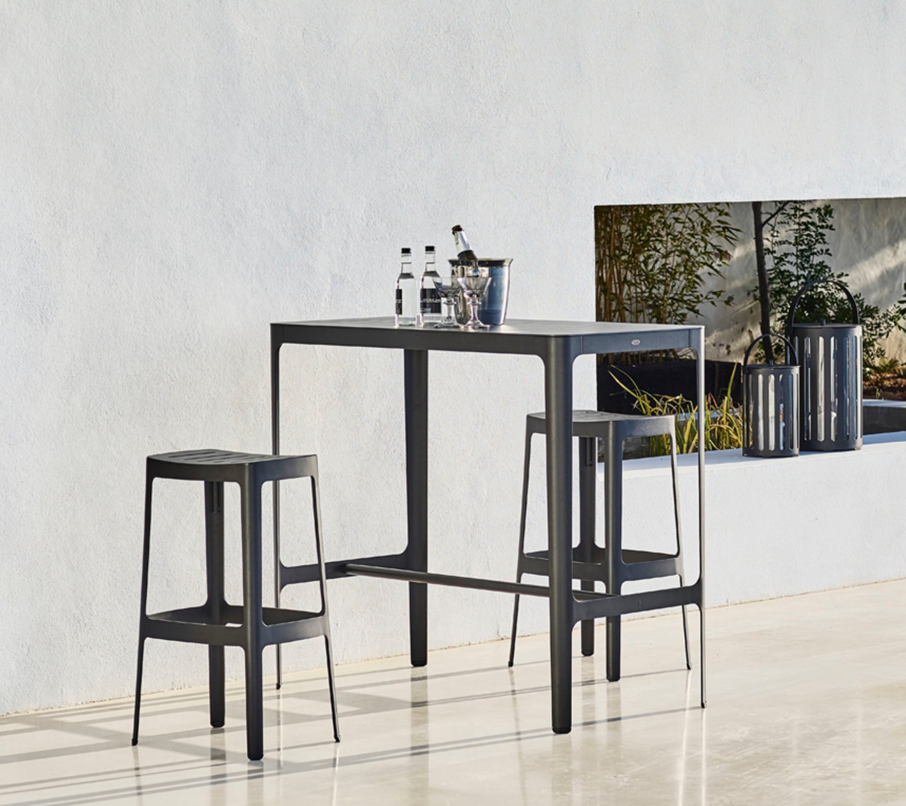 Ett stilrent bord med två matchande pallar, med en minimalistisk design och flaskor placerade ovanpå, mot en neutral bakgrund.