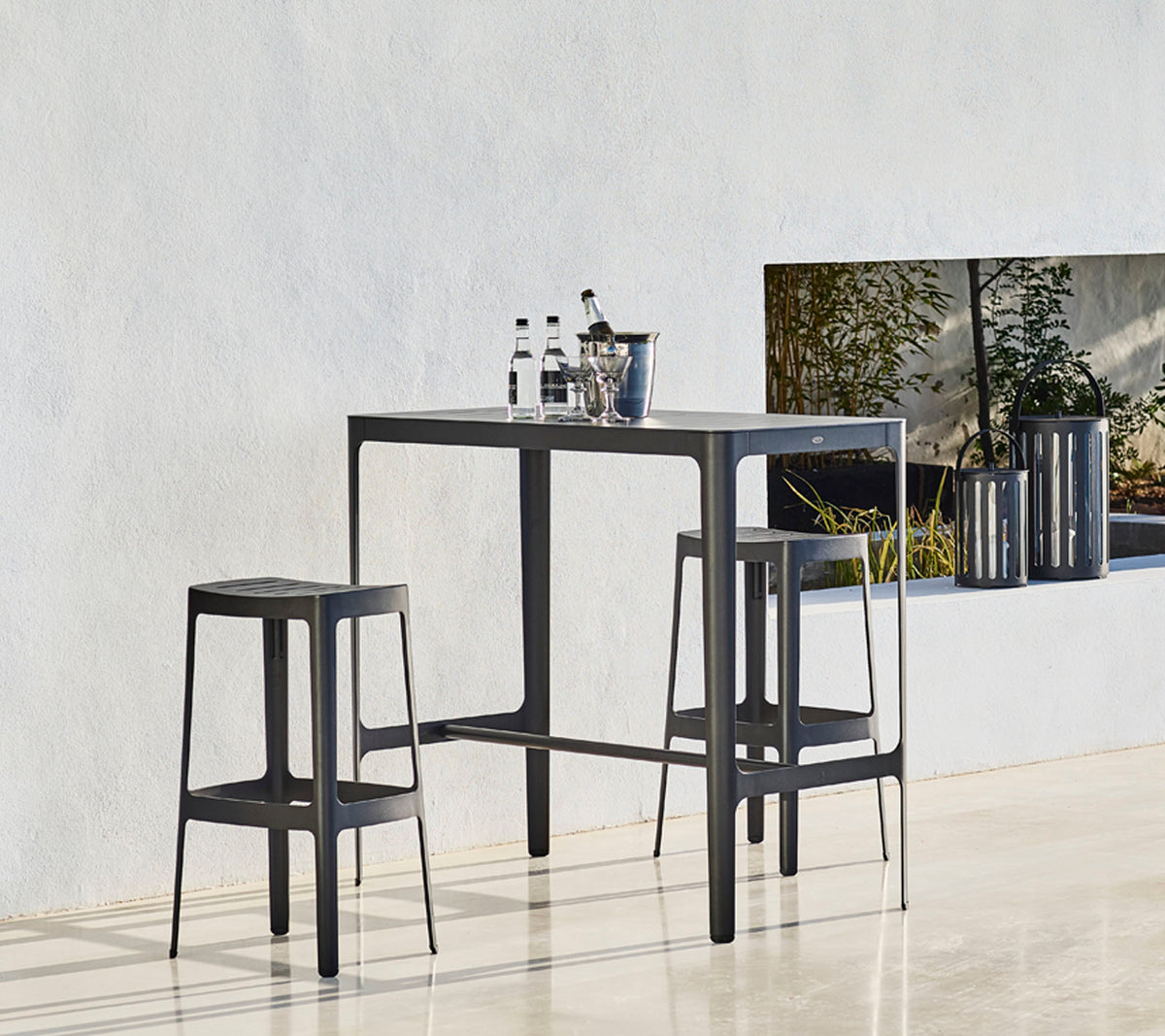 Ett stilrent bord med två matchande pallar, med en minimalistisk design och flaskor placerade ovanpå, mot en neutral bakgrund.