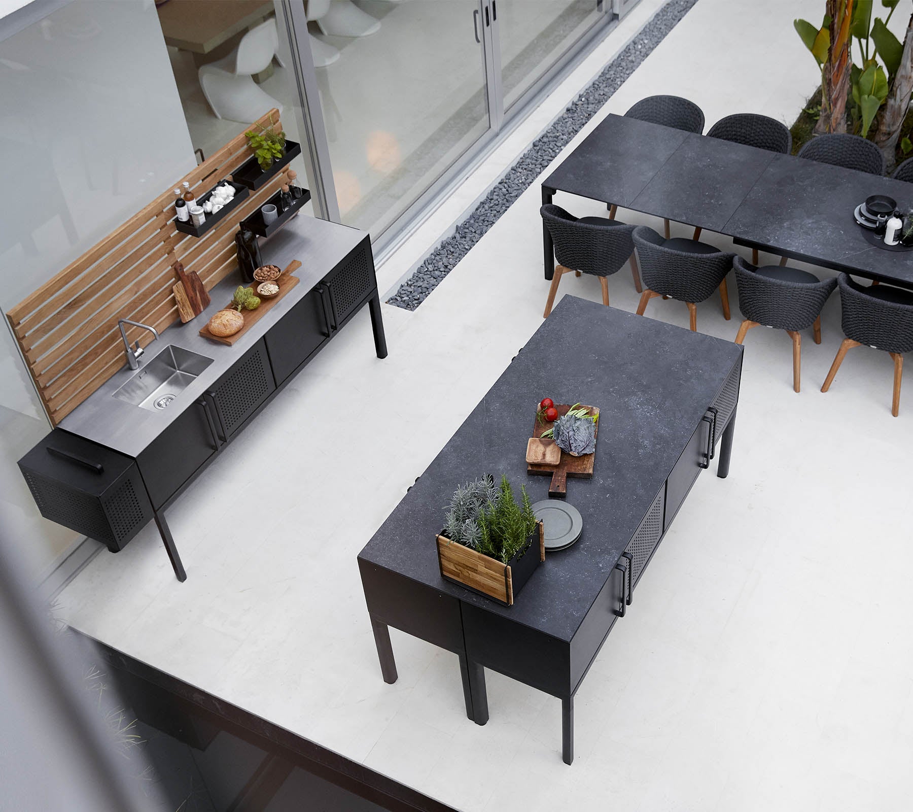 Modern uteköksuppställning med en elegant bänkskiva, rymligt matbord och stiliga sittplatser med växter och dekorativa element.