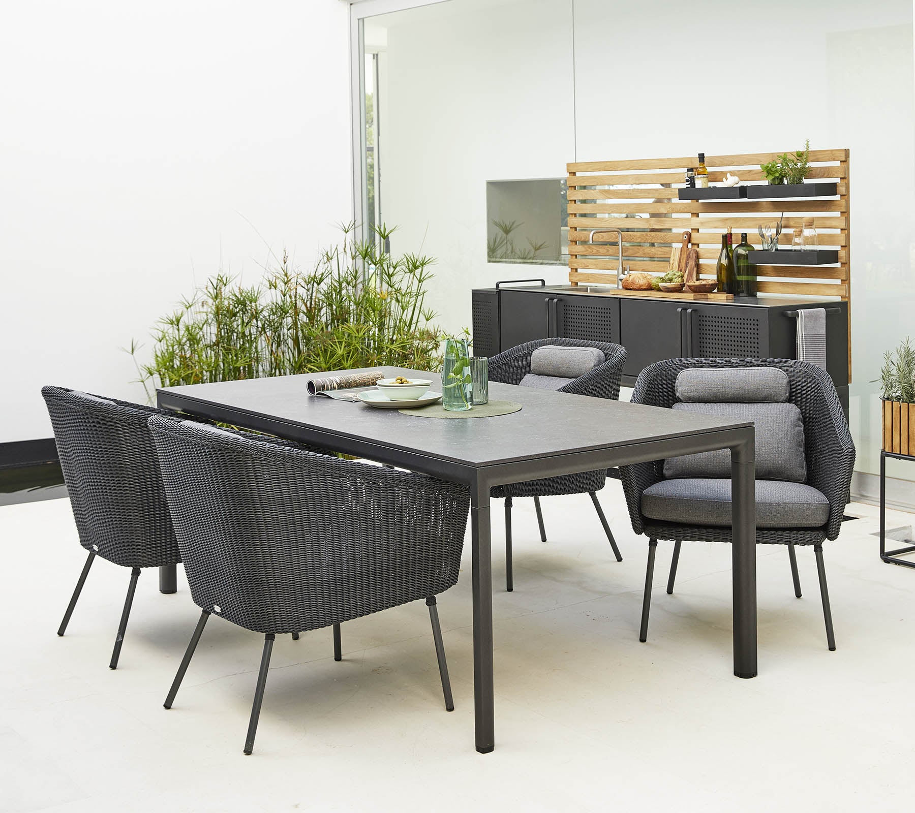 Stiligt utomhusmatgrupp som har ett slankt bord och bekväma, moderna stolar omgivna av dekorativ grönska.