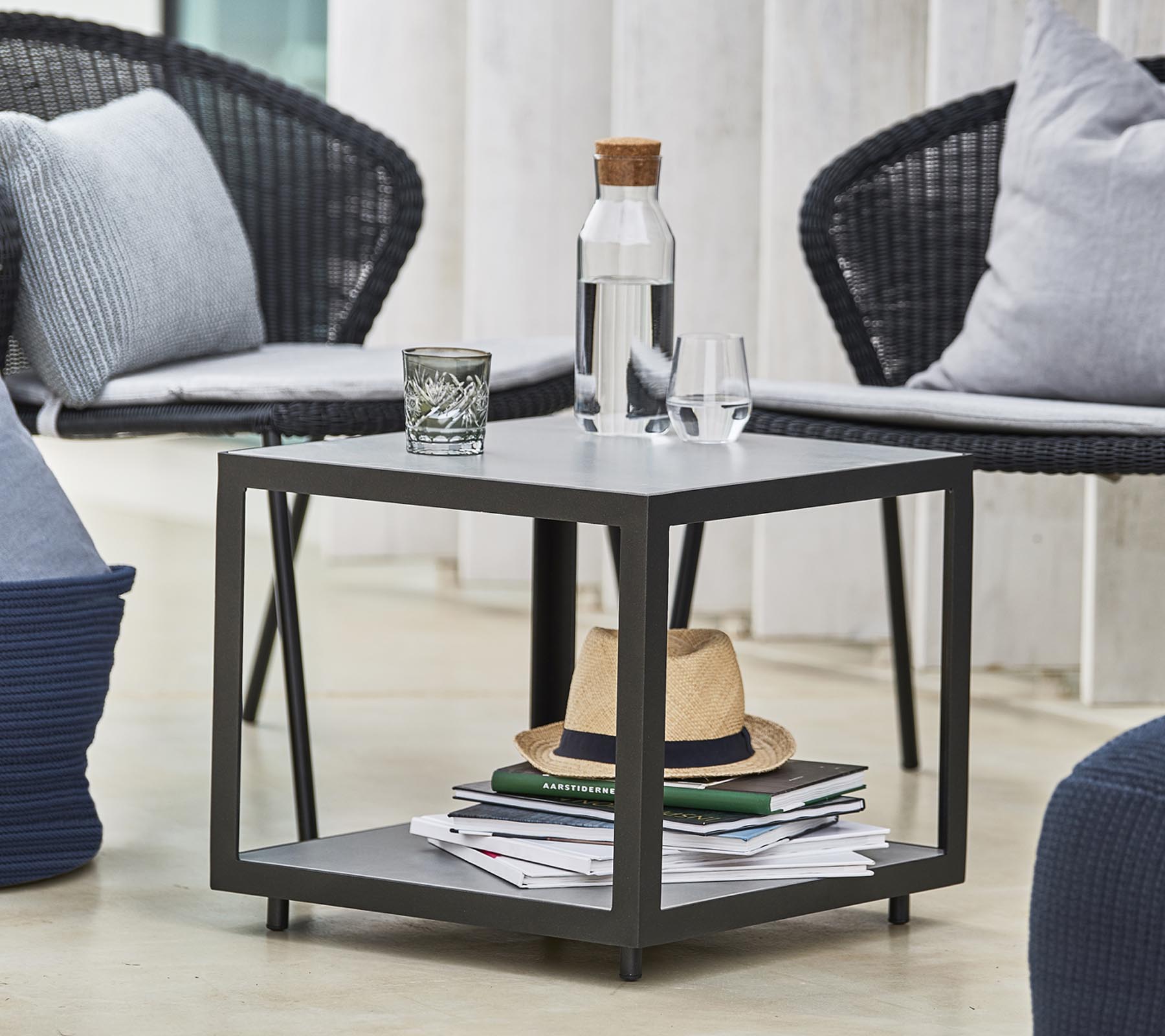 Ett modernt bord med en vattenflaska, ett glas och dekorativa föremål, omgiven av stiliga stolar och kuddar.