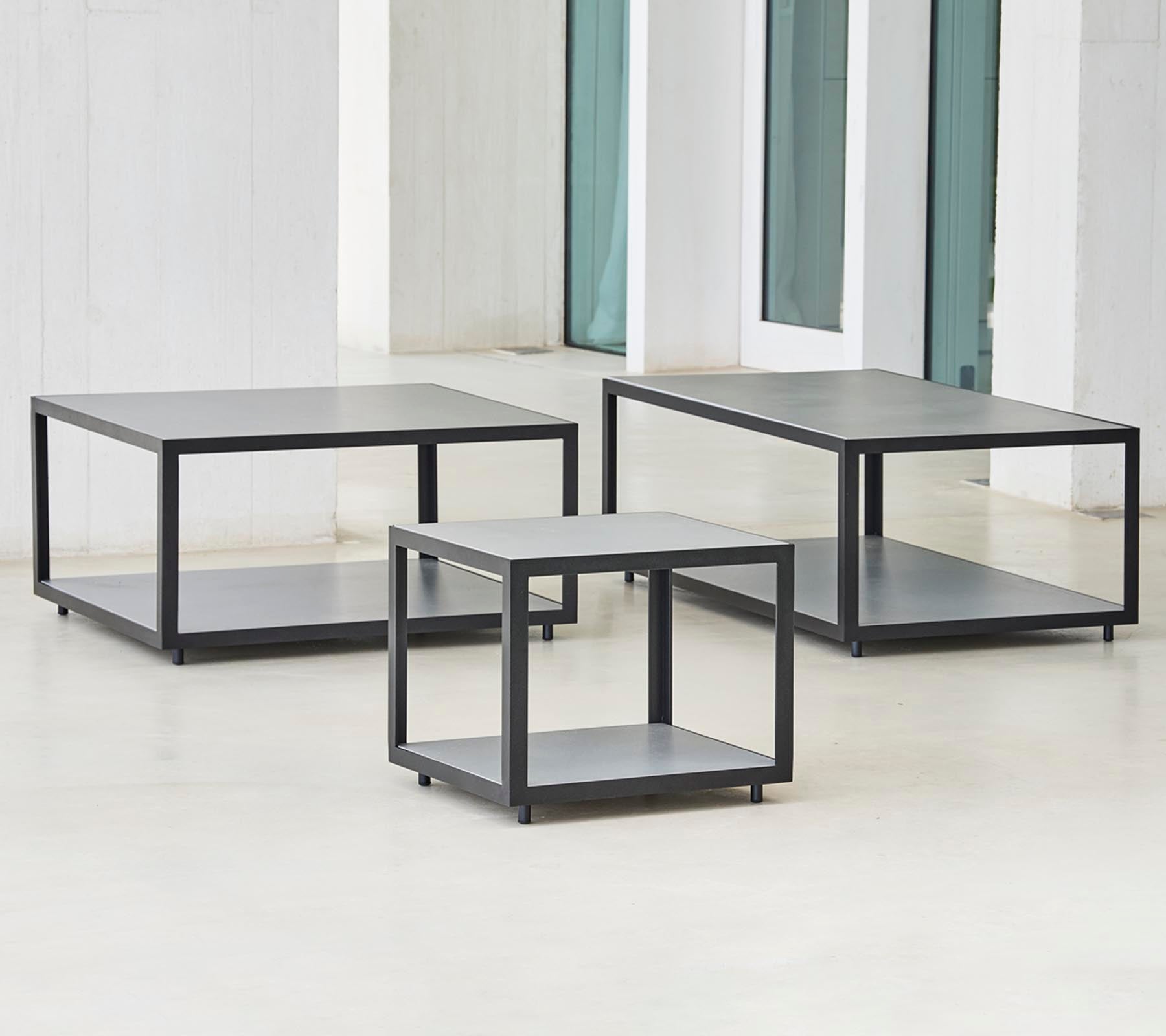 Tre moderna bord med en minimalistisk design, som har en slank ram och flera nivåer för förvaring eller visning.