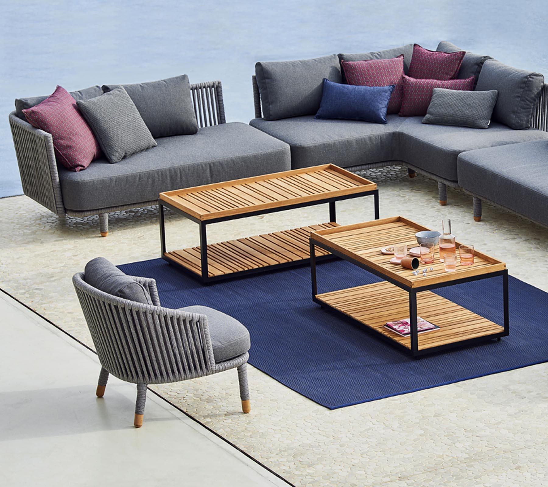 Modern sittarrangemang med en grå sektionsoffa, en stilren rund stol och träkaffebord med en blå matta under.