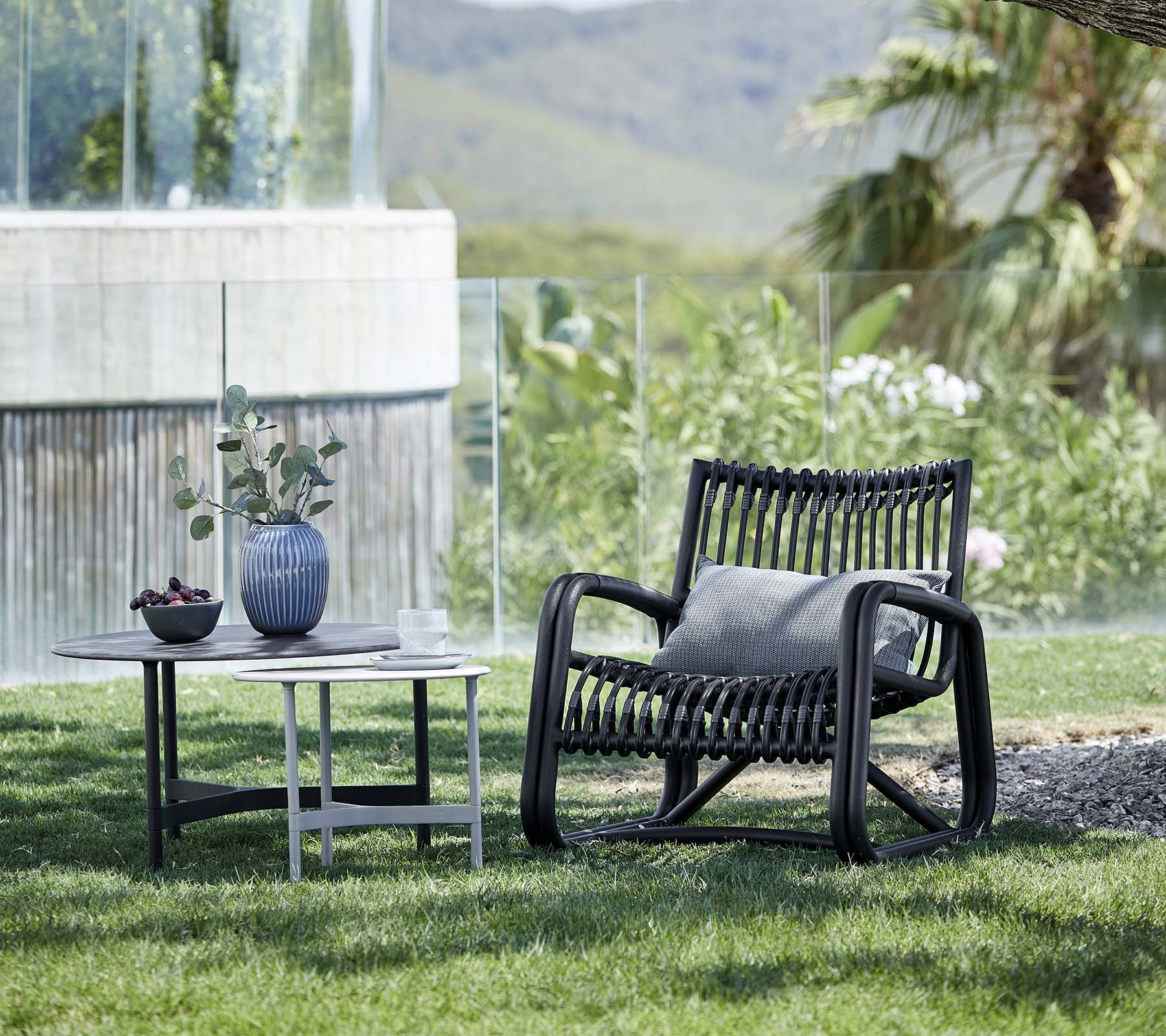 Nutida loungestol med ett mönstrat mönster, tillsammans med ett sidobord som håller en vas och en krukväxt, placerad i ett naturlandskap.