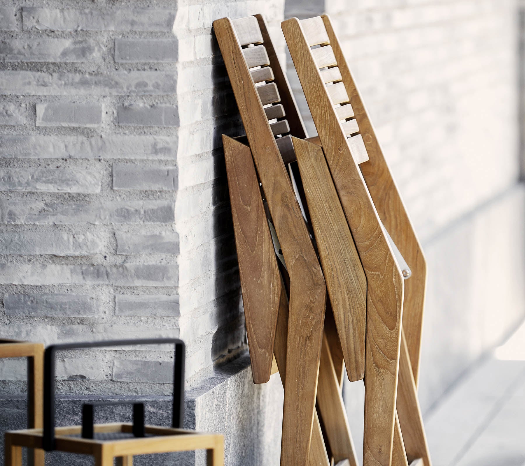 Tre trästativ med en elegant design, lutande mot en strukturerad vägg, i sällskap av en enkel, stilren stol i förgrunden.