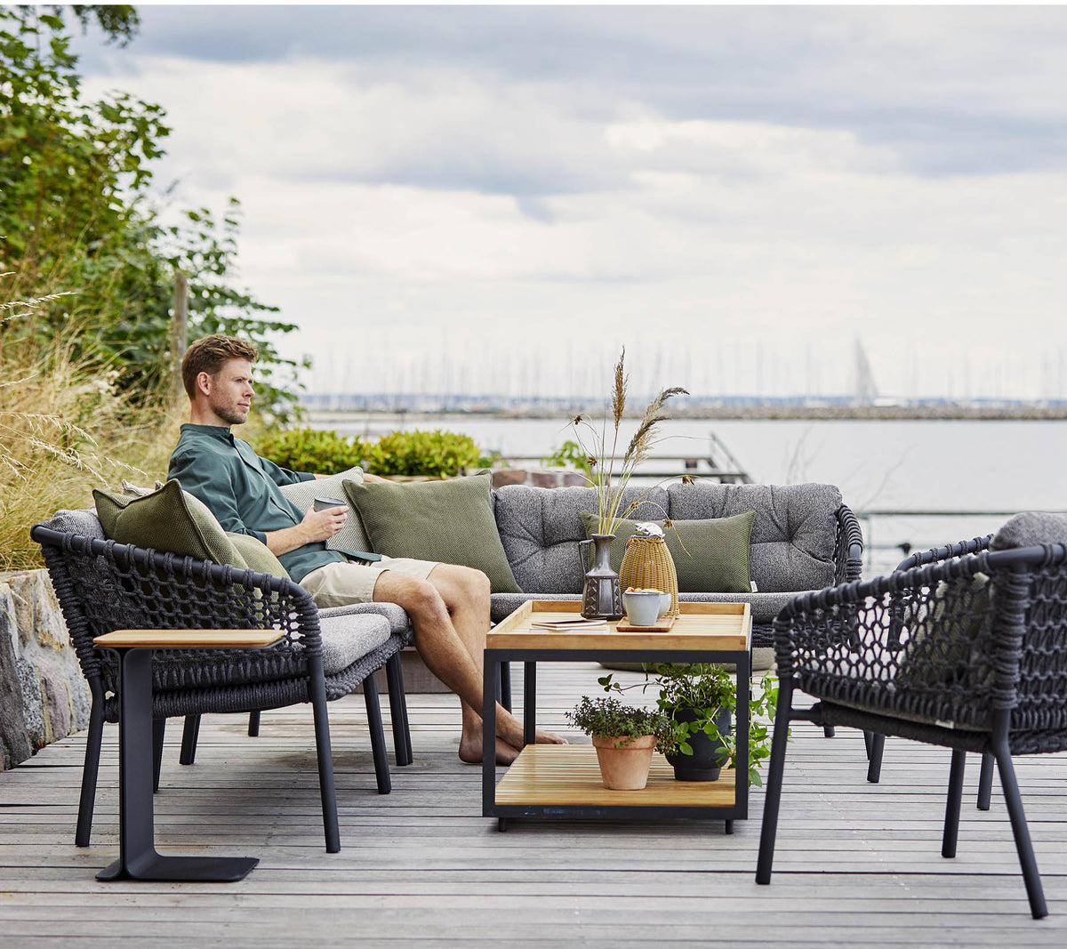 Ett bekvämt sittområde med en man som kopplar av, med stiliga flätade fåtöljer och ett träkaffebord prytt med växter och dekorativa föremål.
