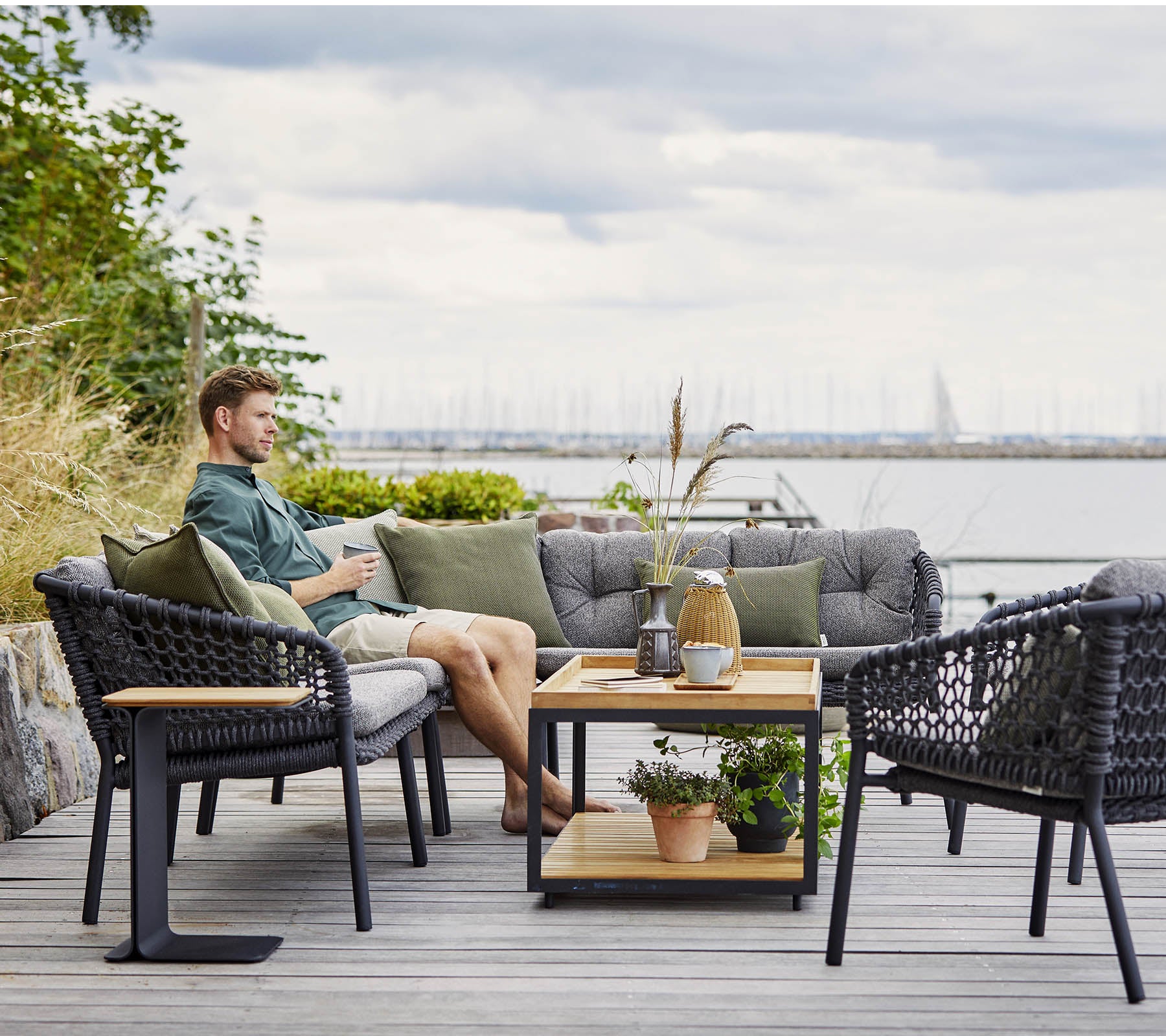 Ett bekvämt sittområde med en man som kopplar av, med stiliga flätade fåtöljer och ett träkaffebord prytt med växter och dekorativa föremål.