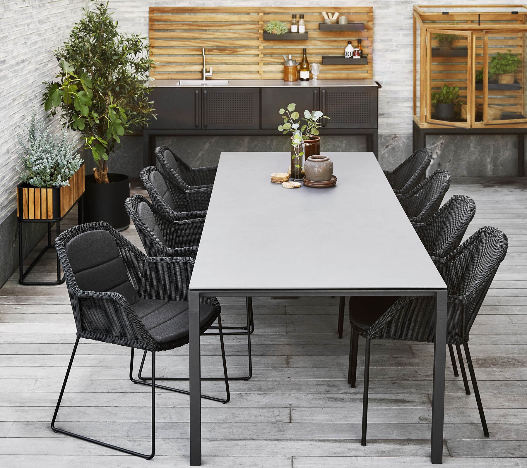En modern matplats med ett långt bord omgiven av stiliga svarta stolar, kompletterat med dekorativa växter och en träbakgrund.