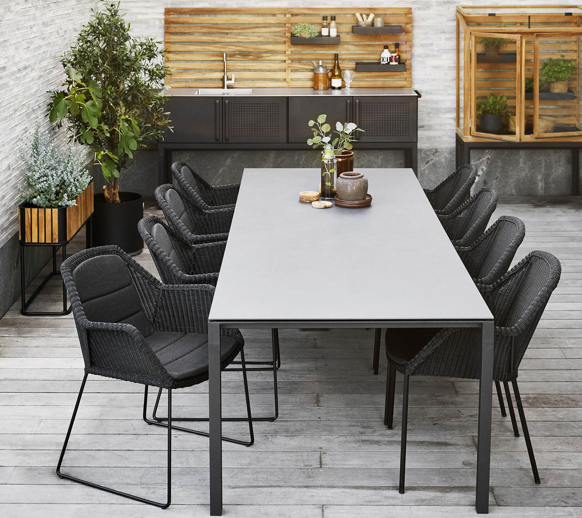 En modern matplats med ett långt bord omgiven av stiliga svarta stolar, kompletterat med dekorativa växter och en träbakgrund.