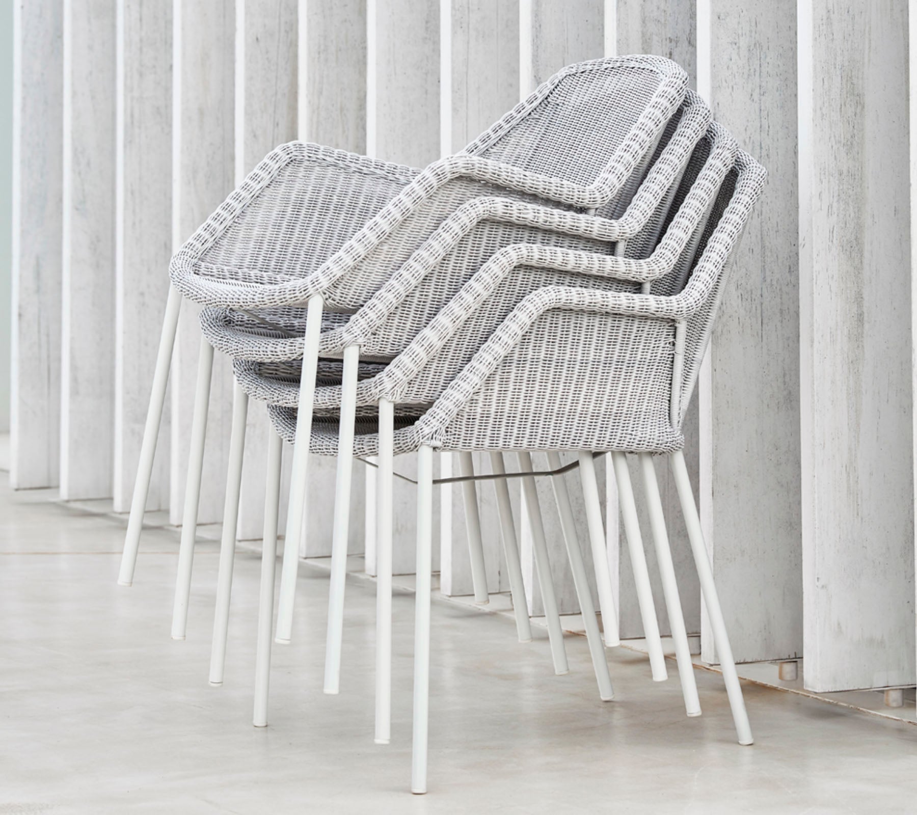 Staplade moderna stolar med en vävd design i grått och vitt, som lutar mot vertikala ytor och visar en elegant och minimalistisk estetik.