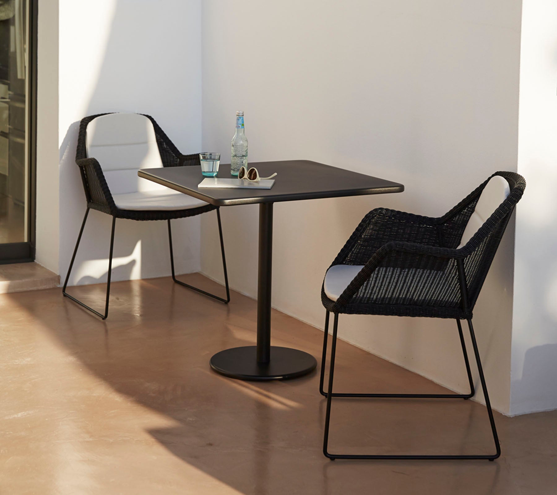Modernt bord med två stiliga svarta stolar, ackompanjerat av en vattenflaska och solglasögon, placerat mot en minimalistisk bakgrund.