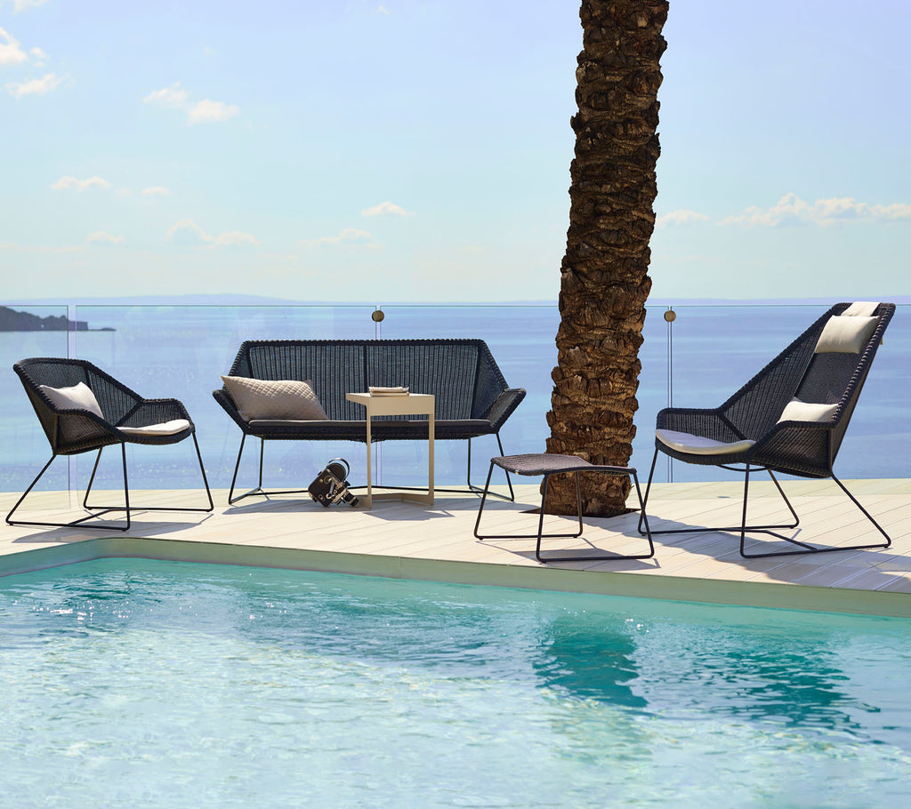 Modern lounge-sittplatser med svarta stolar och en loveseat bredvid en pool.