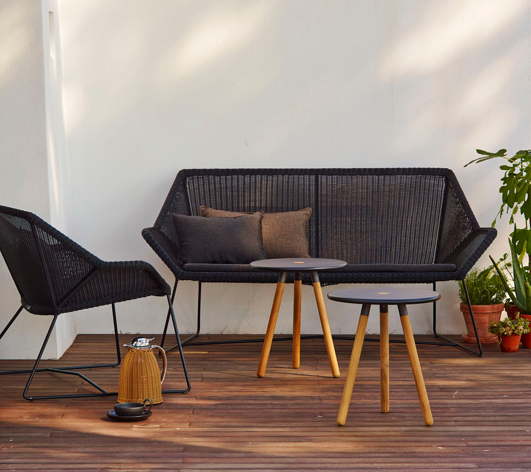 Modernt sittarrangemang med en svart soffa med kuddar, en matchande stol och ett runt bord med träben.