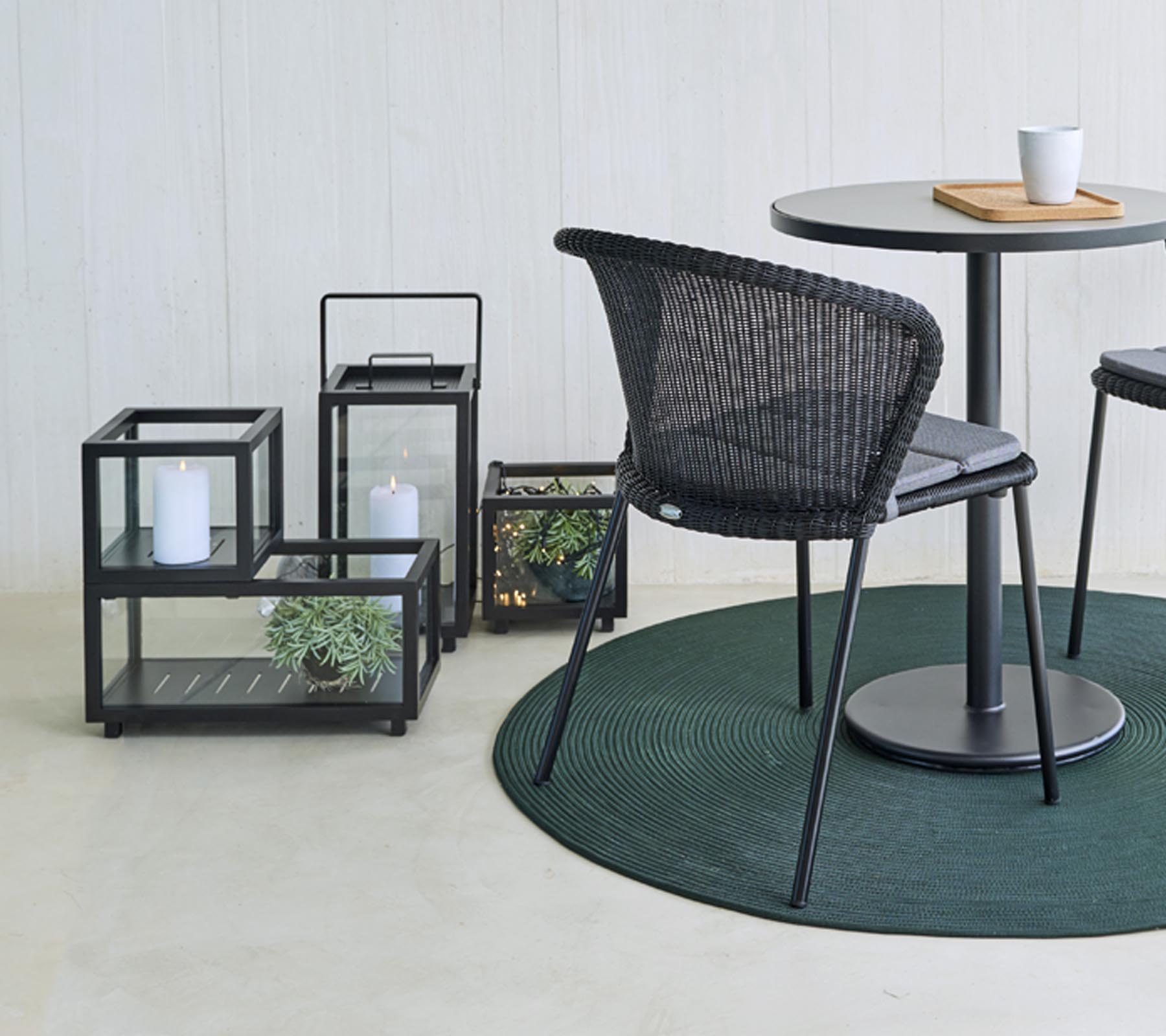 Moderna sittplatser och dekorativa glaslyktor med växter, arrangerade runt ett runt bord, på en rund grön matta.