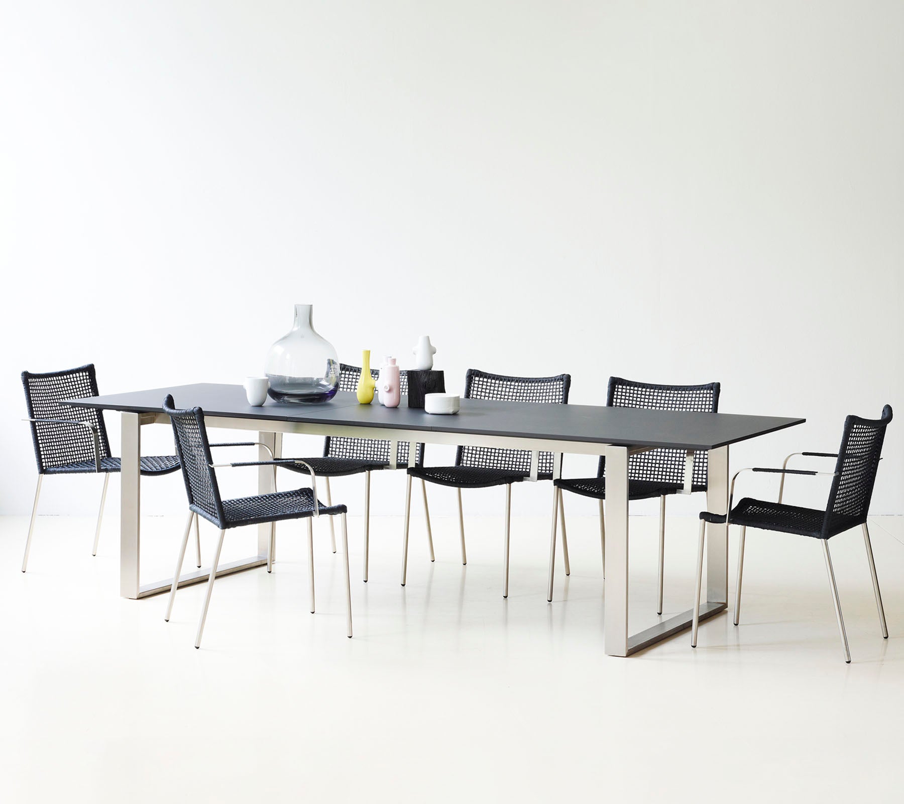 Ett modernt matbord med sleek design, omgiven av stiliga svarta nätstolar och dekorativa vaser.