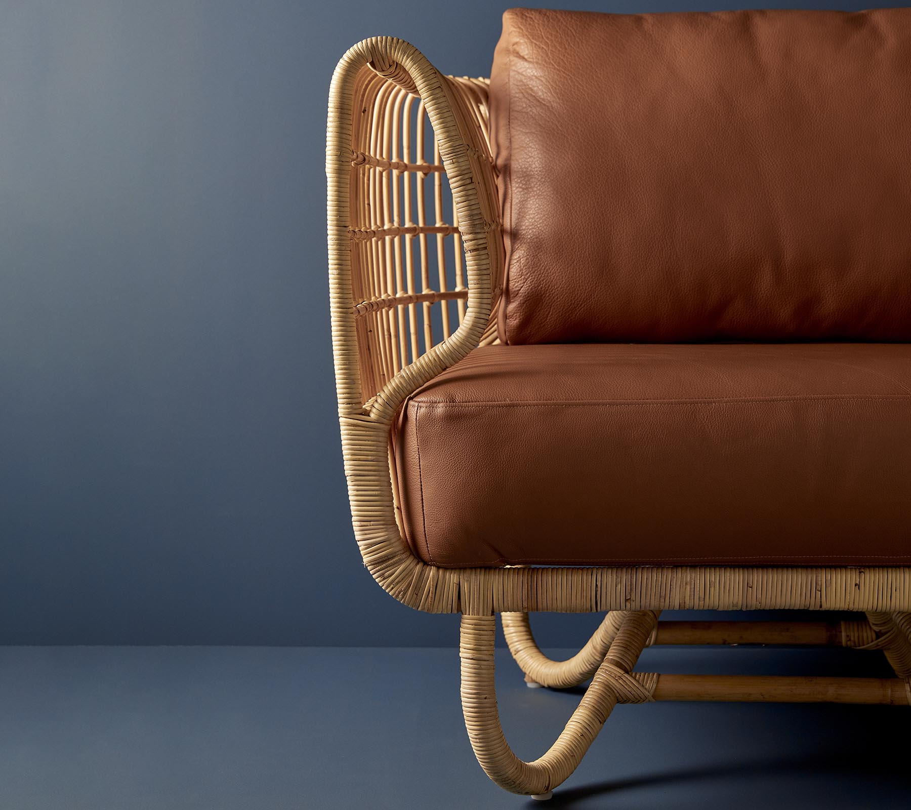 Rattanstol med en böjd design och bruna läderkuddar, som visar en blandning av naturliga material och modern estetik.