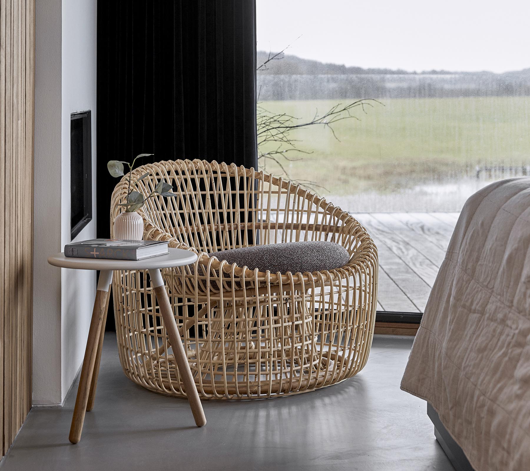 En stilren vävd stol i kombination med ett litet sidobord, placerad i en lugn miljö med stora fönster som släpper in naturligt ljus.