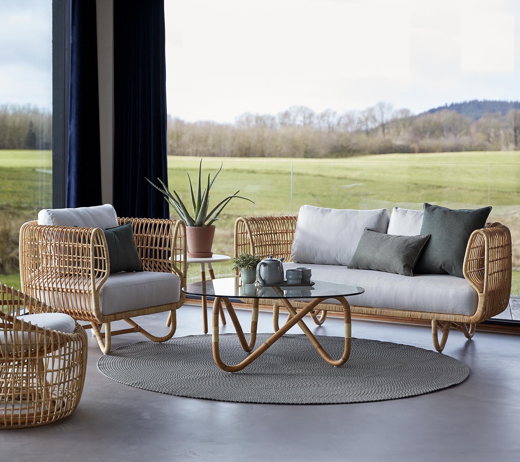 En stilren sittgrupp med vävda möbler, en rund matta och ett glasskaffebord, kompletterat med minimalistiska dekorationsinslag.