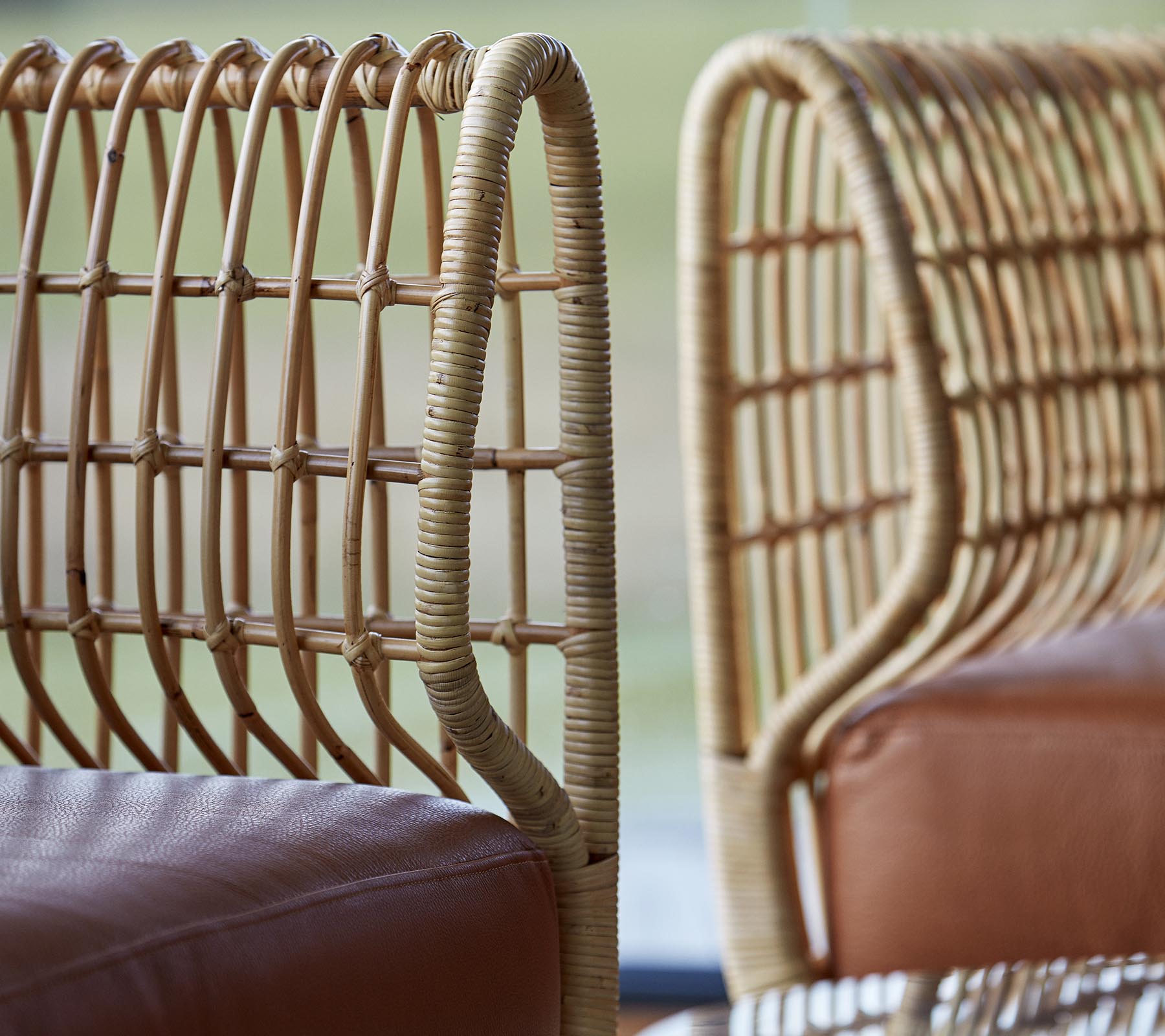 Två stiliga stolar med vävda rottingryggar och släta lädersäten, som visar en modern designestetik.