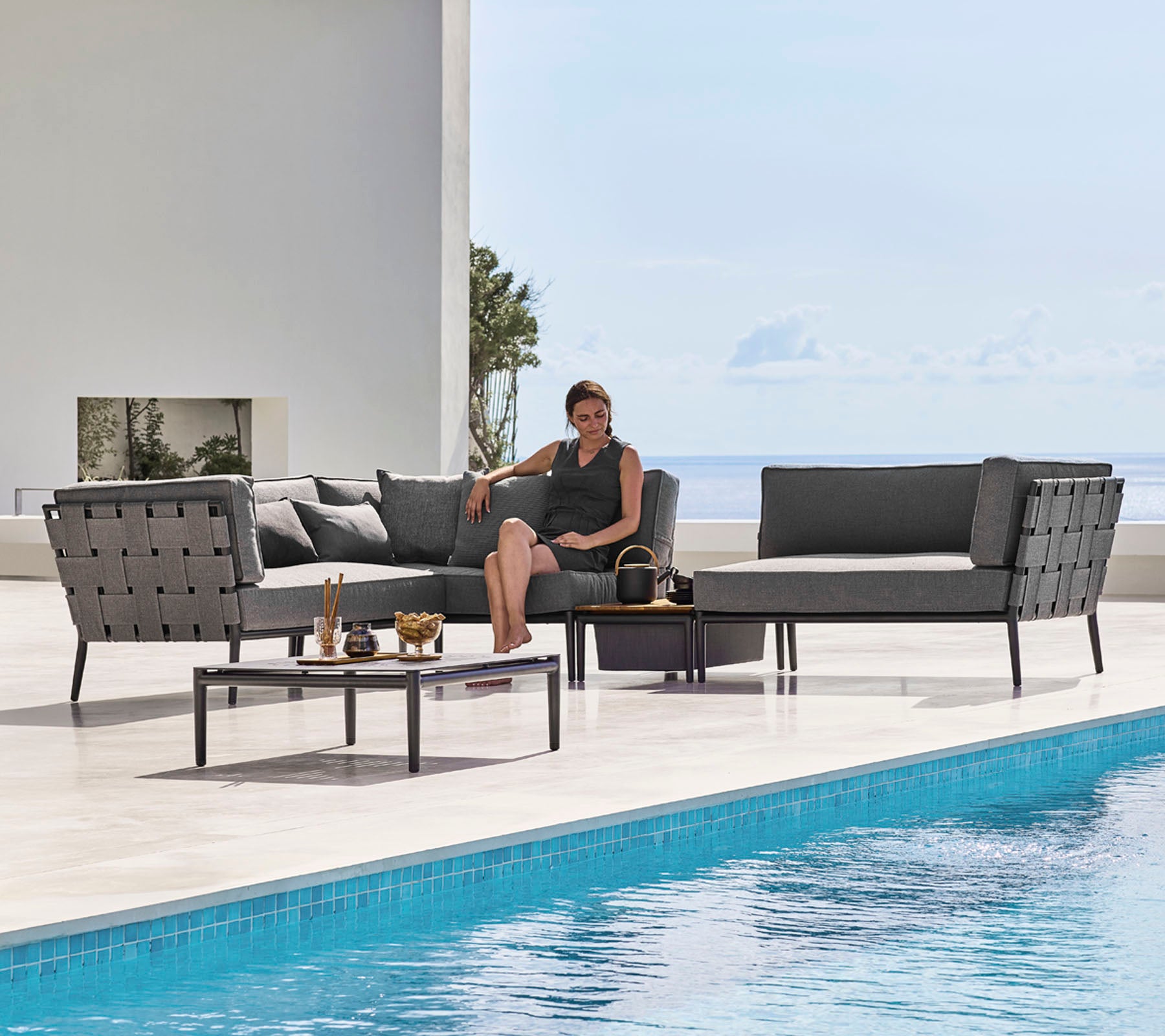 Ett stiligt utemöbelset med snygga sittplatser och ett glasbords vid en pool, med en person som kopplar av bekvämt.