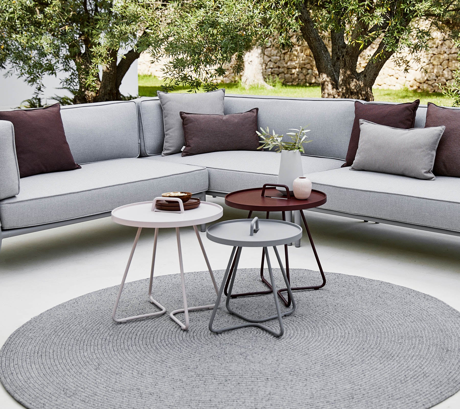 Stilfullt utrymme utomhus med en sektionsoffa med kuddar och moderna runda soffbord i en avslappnad, modern miljö.