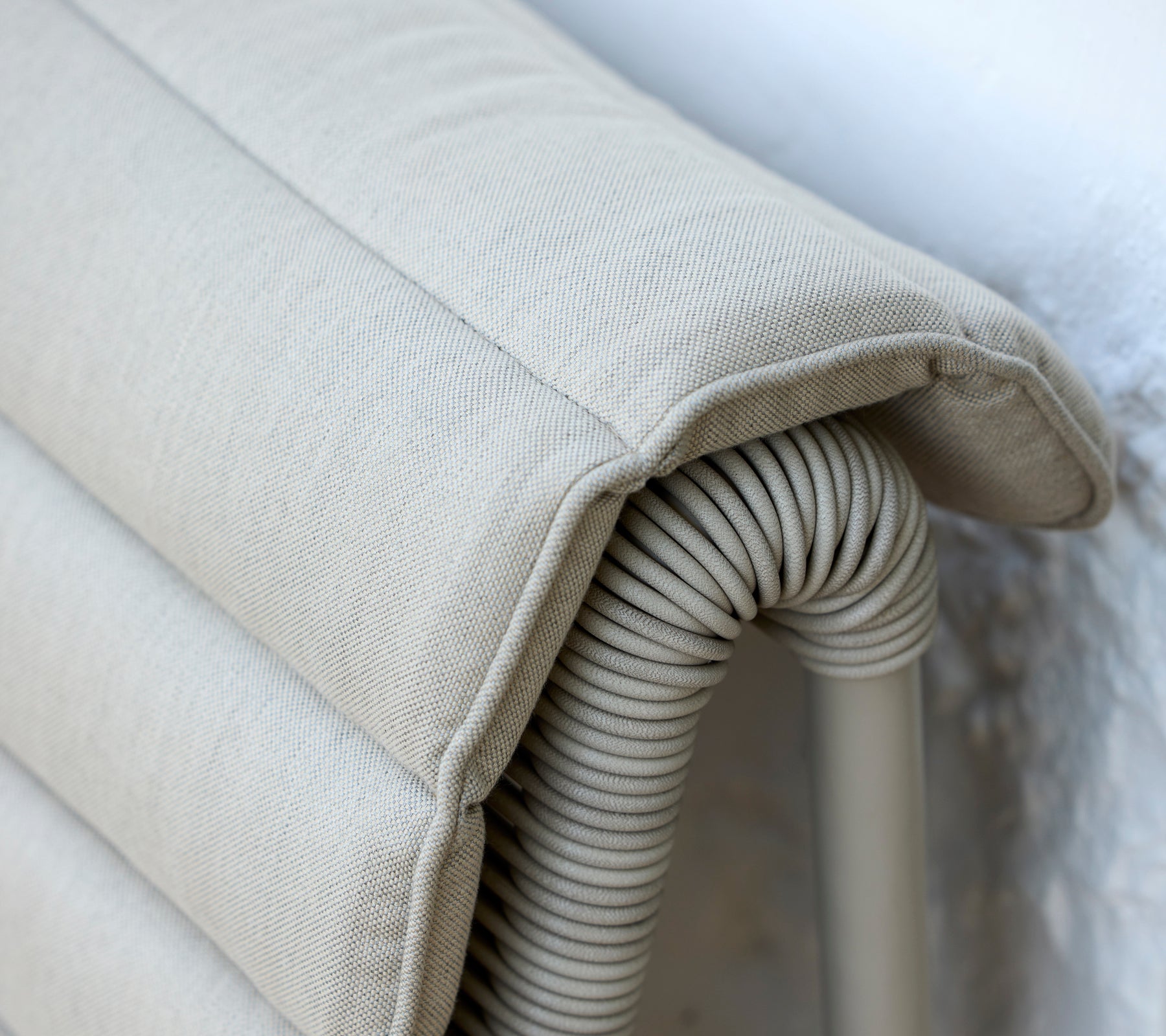 Beige kudde med ribbad textur som vilar mot en ljus vägg.