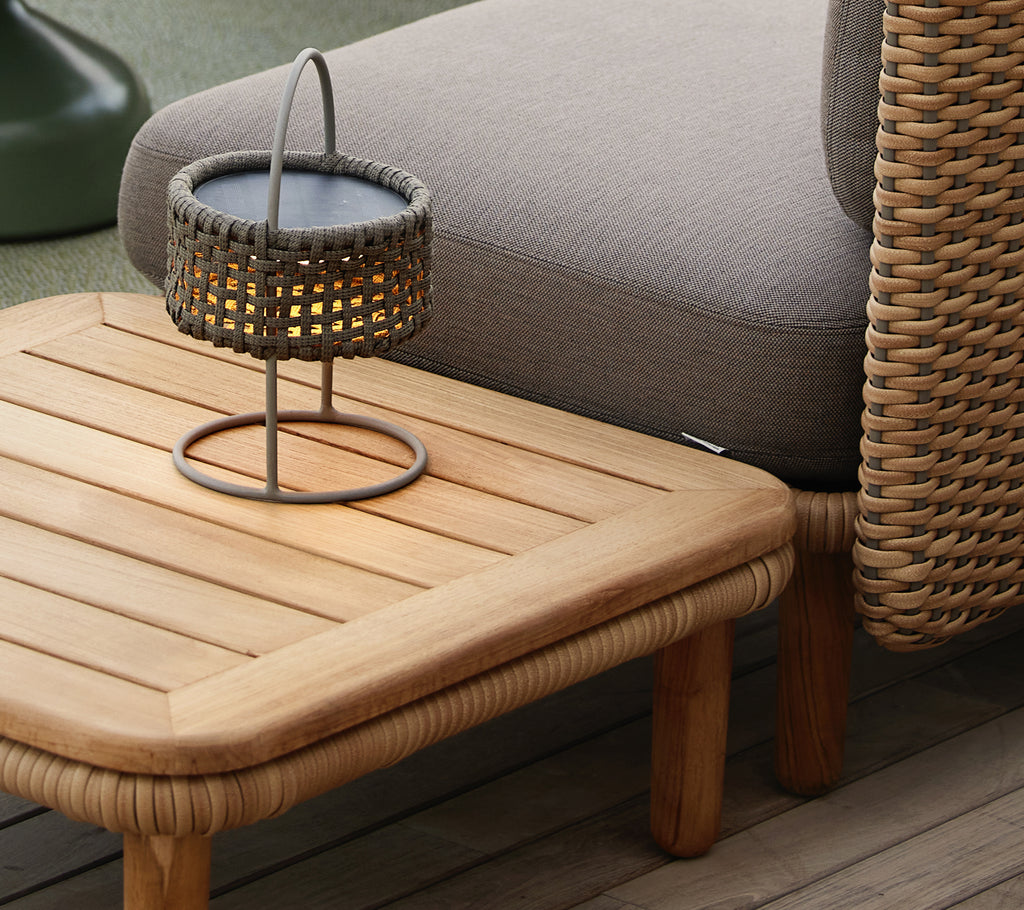 Teak kaffebord med en ribbad topp, åtföljt av en vävd lampa som skapar en mysig och inbjudande atmosfär.