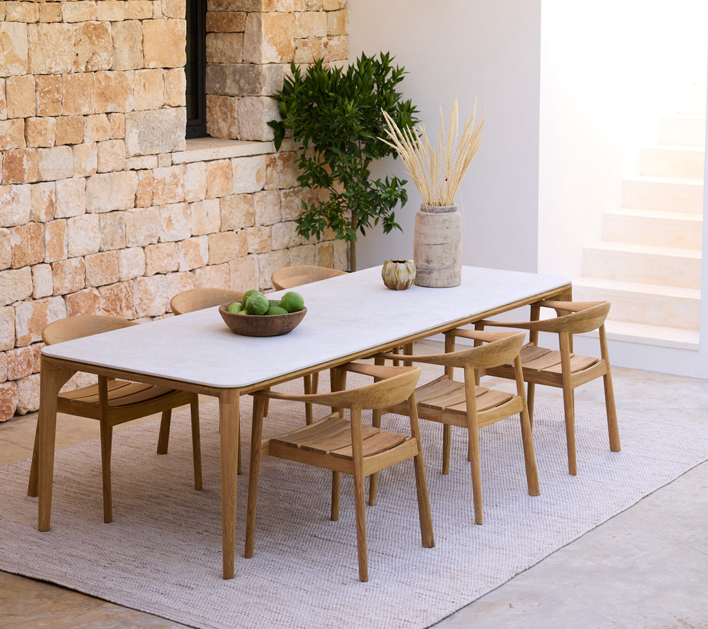 Moderna matplats med ett vitt bord och trästolar mot en stenvägg.