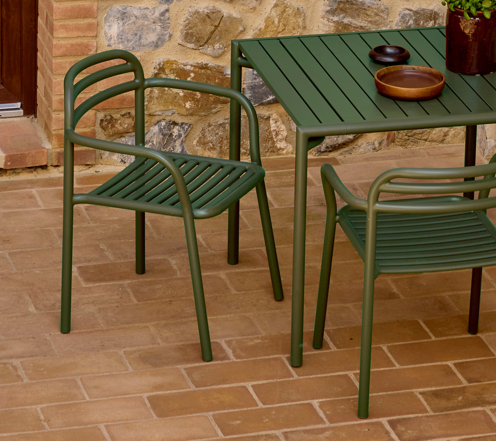 Green Bliss armchair next to a matching table, featuring a minimalist design and a relaxed aesthetic, set on a textured surface.