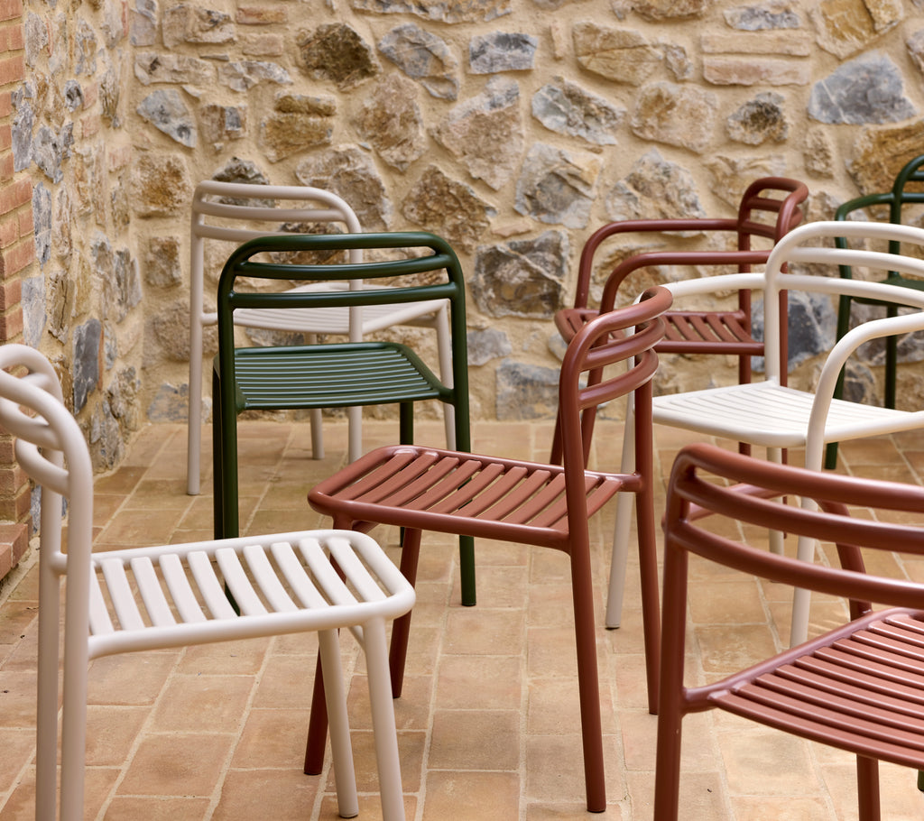 A collection of Bliss chairs in dark green, desert red, and sand colors arranged against a stone wall.