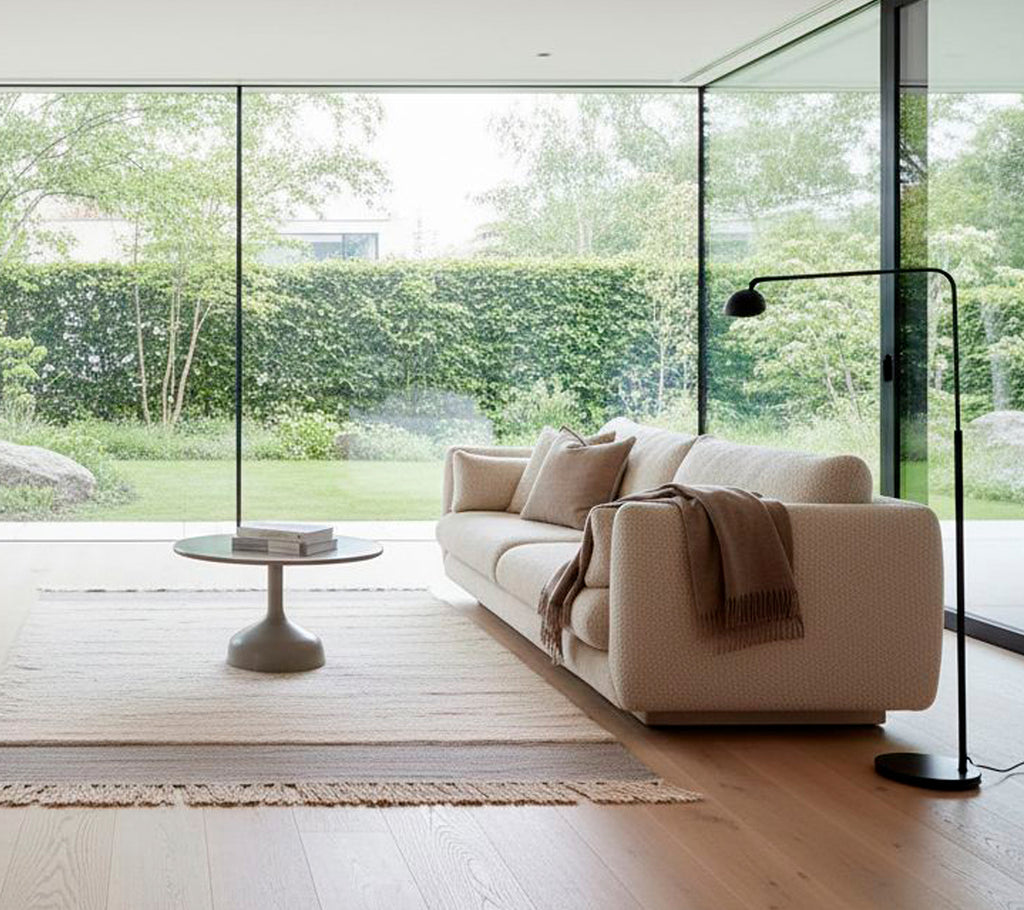 Modern vit soffa med en svart golvlampa och runt soffbord i ett minimalistiskt vardagsrum.