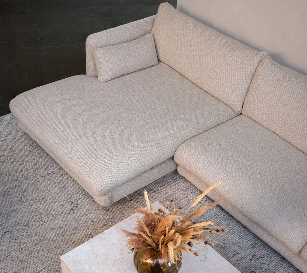 Modern beige soffa med ett vitt bord och en dekorativ vas i en stilren loungeinredning.