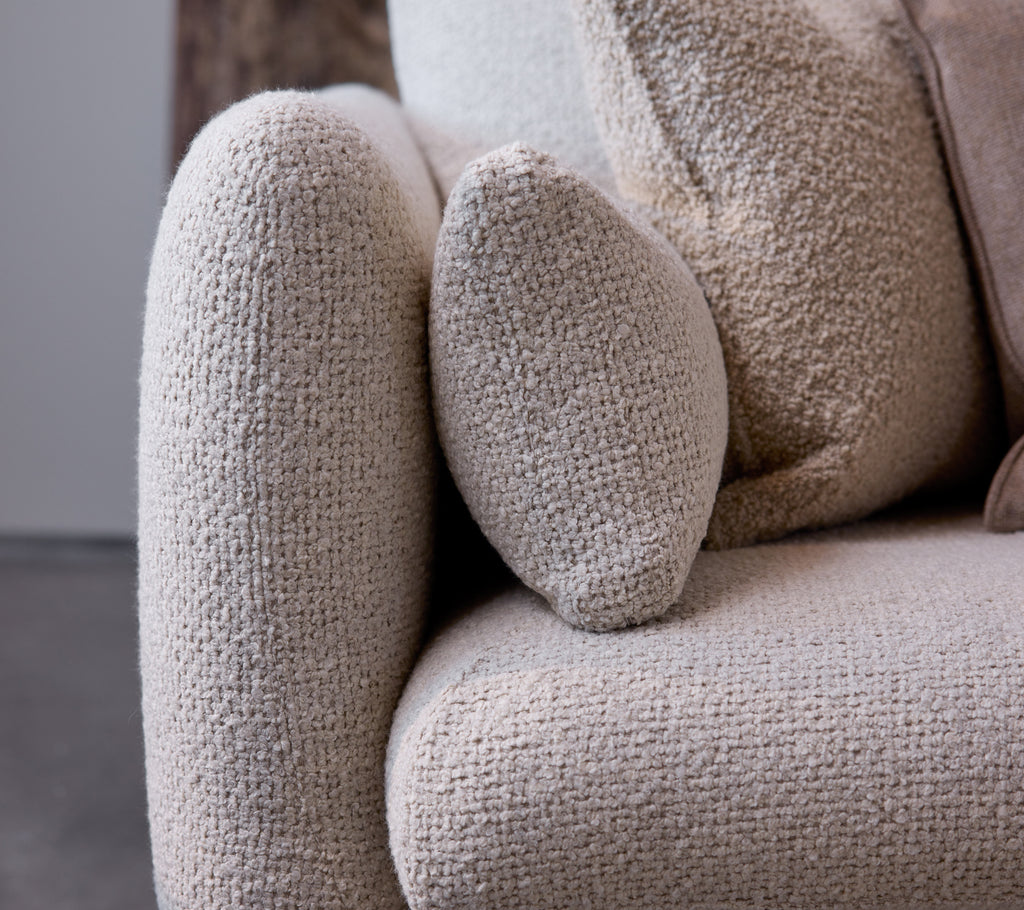 Närbild av armstödet på en Bloom-soffa i en sandfärgad textur, som visar en rundad design och mjukt, mysigt tyg.