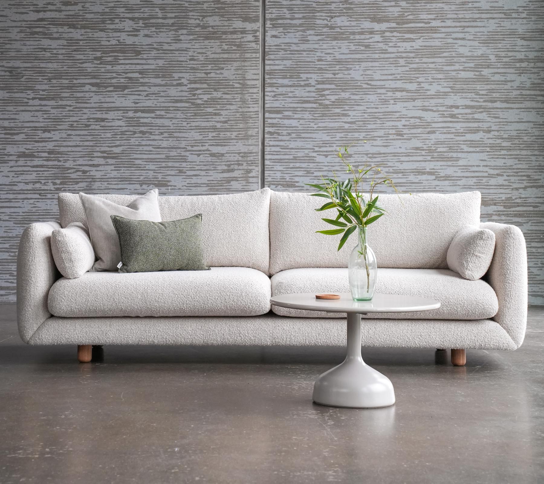 En stilren soffa med kuddar bredvid ett Glaxe soffbord med rund topp och eleganta teakben, prytt med en vas med blommor.