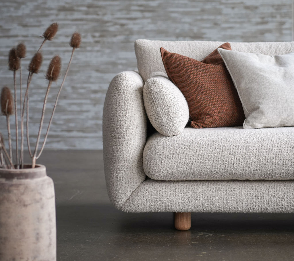Mysig soffa med blomstersoffa, teakben och lyftkuddar, i sällskap av en dekorativ vas och torkade blommor. Elegant och inbjudande design.