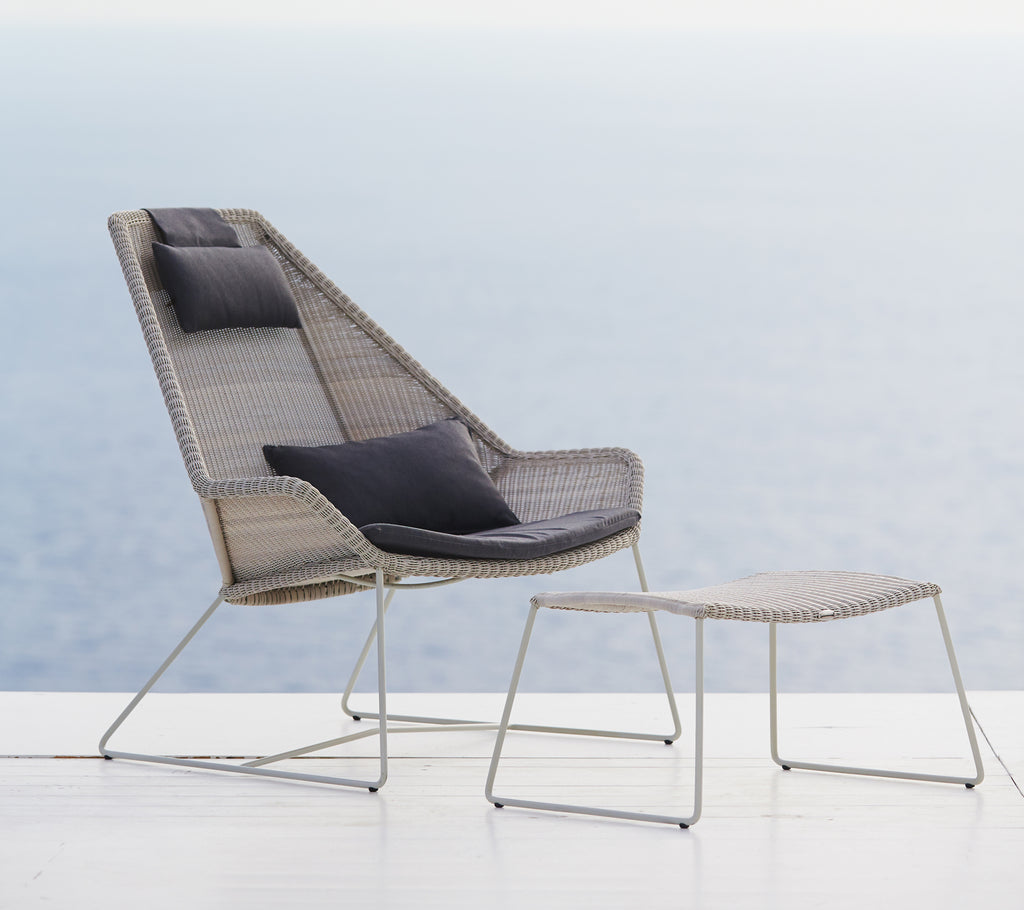 Modern grå stol med svart kudde och grå pouf mot en naturskön bakgrund.
