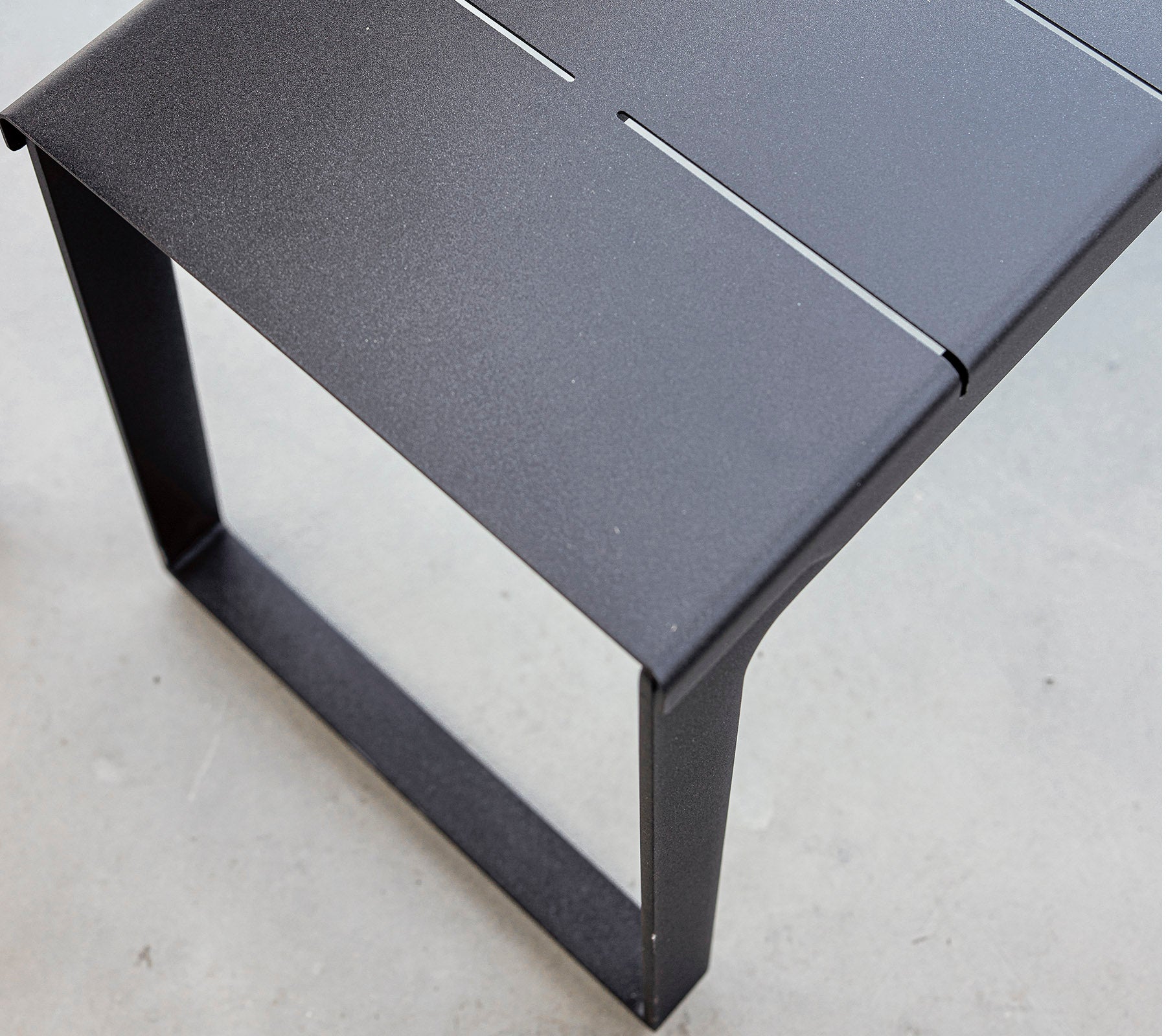 Svart metallbord med en strömlinjeformad design och minimalistisk estetik, med en lamellerad topp och stabil ram. Ideal för moderna miljöer.