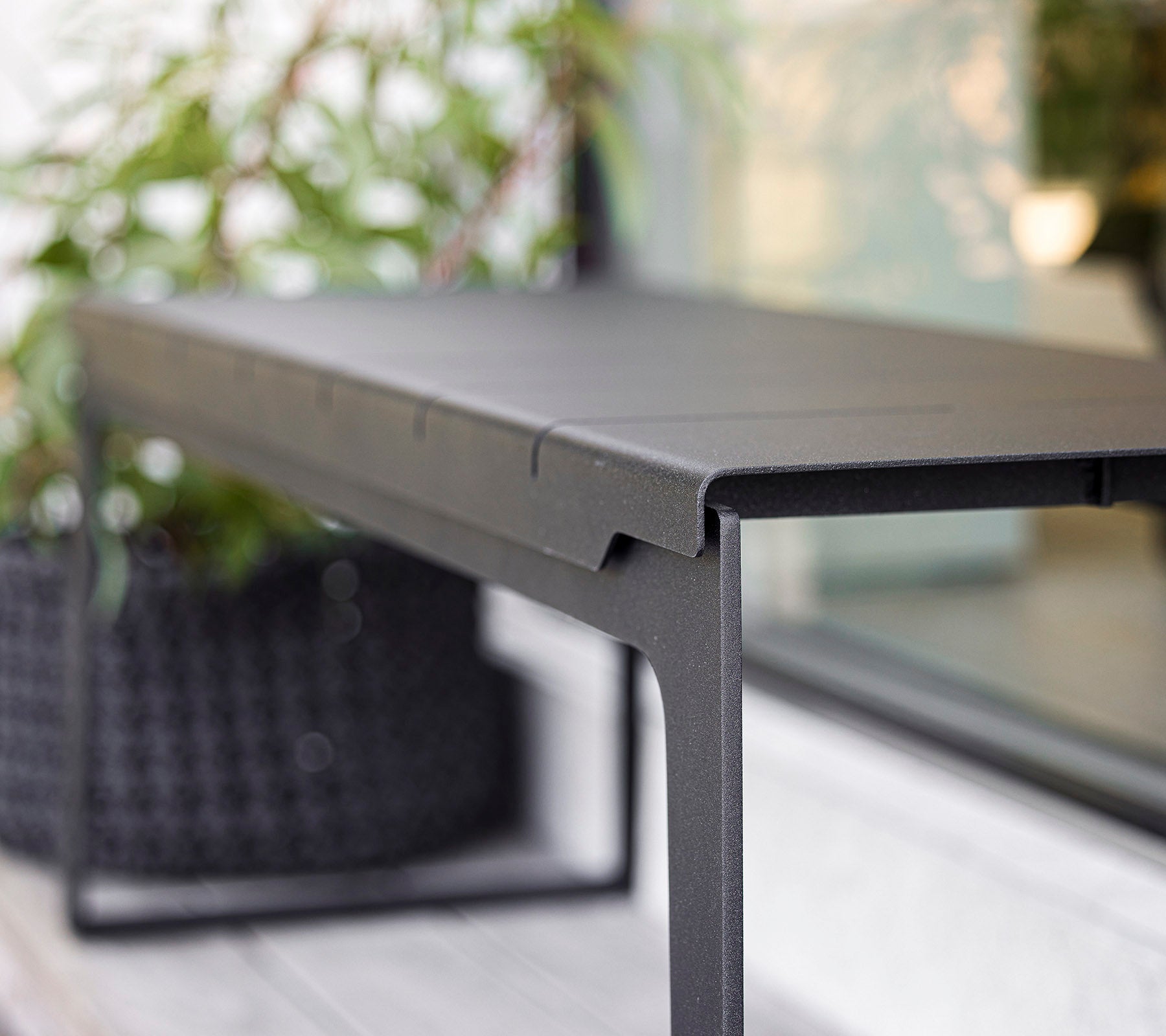 Snyggt svart bord med en minimalistisk design, med rena linjer och en stabil ram, kompletterad av grönska i bakgrunden.