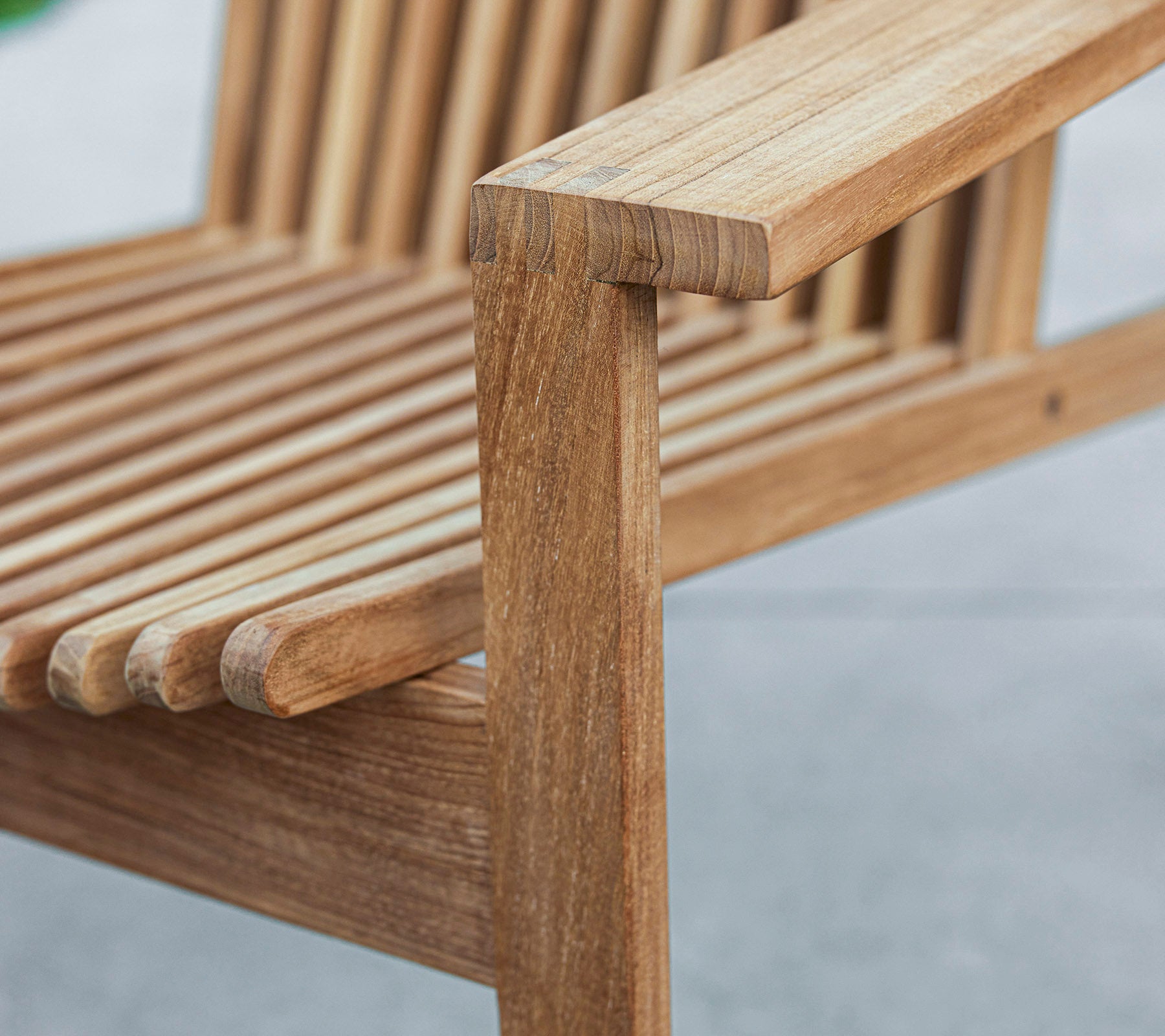 Närbild av en träbänk med ett lameller design och ett robust armstöd, som visar naturligt träådring och hantverk.