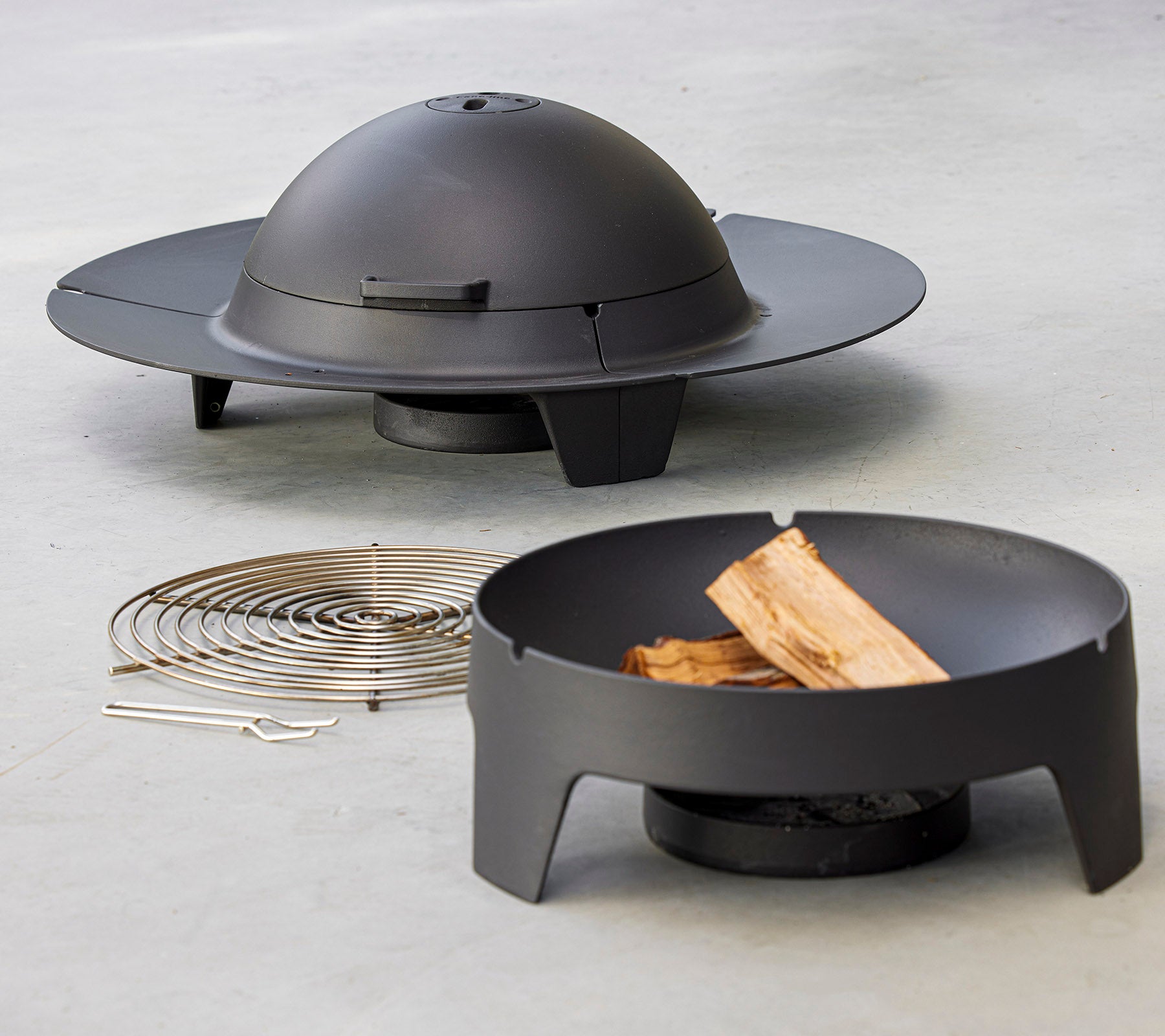 En modern eldstad uppsättning med en slank, cirkulär design med ett kupollock, åtföljd av ett grillgaller och vedbitar.