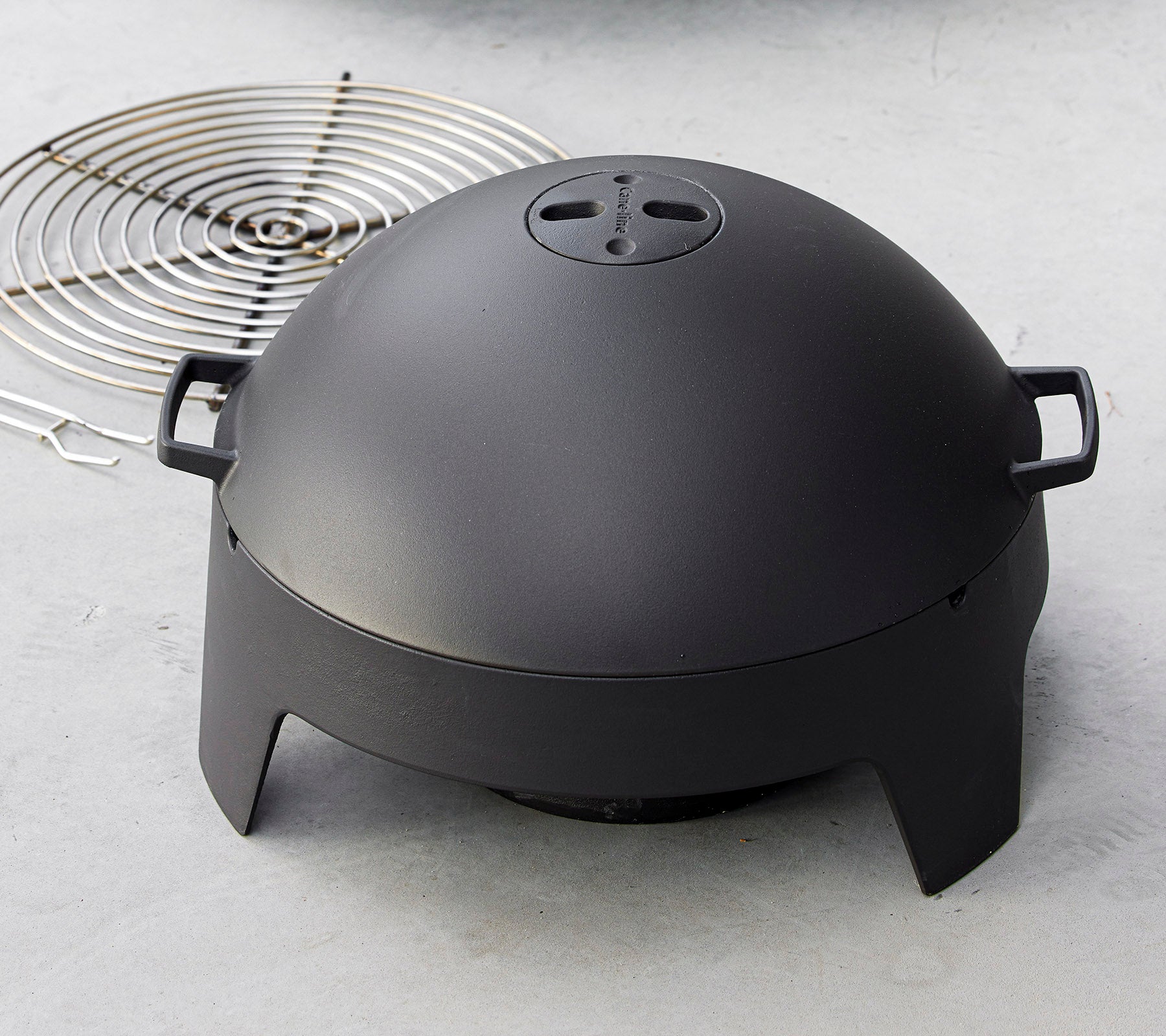 En slank svart matlagningsapparat med kuppelform och handtag, tillsammans med ett cirkulärt grillgaller. Perfekt för grillning och utomhusmatlagning.