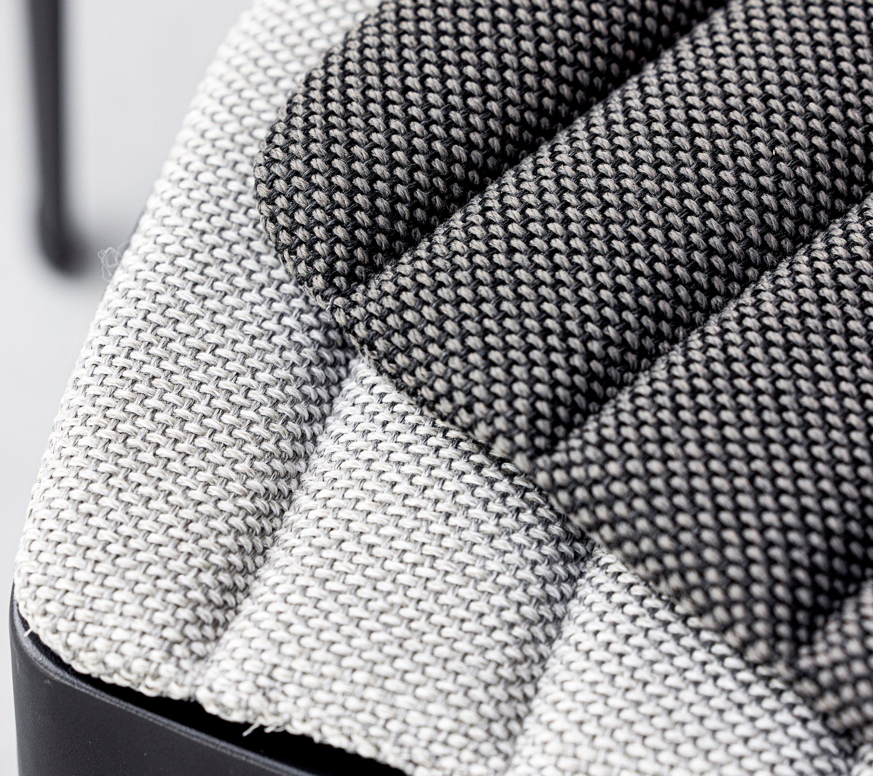 Närbild av en texturerad tygstol, som visar en blandning av ljusa och mörka gråa vävda mönster med en modern design. Idealisk för moderna inredningar.