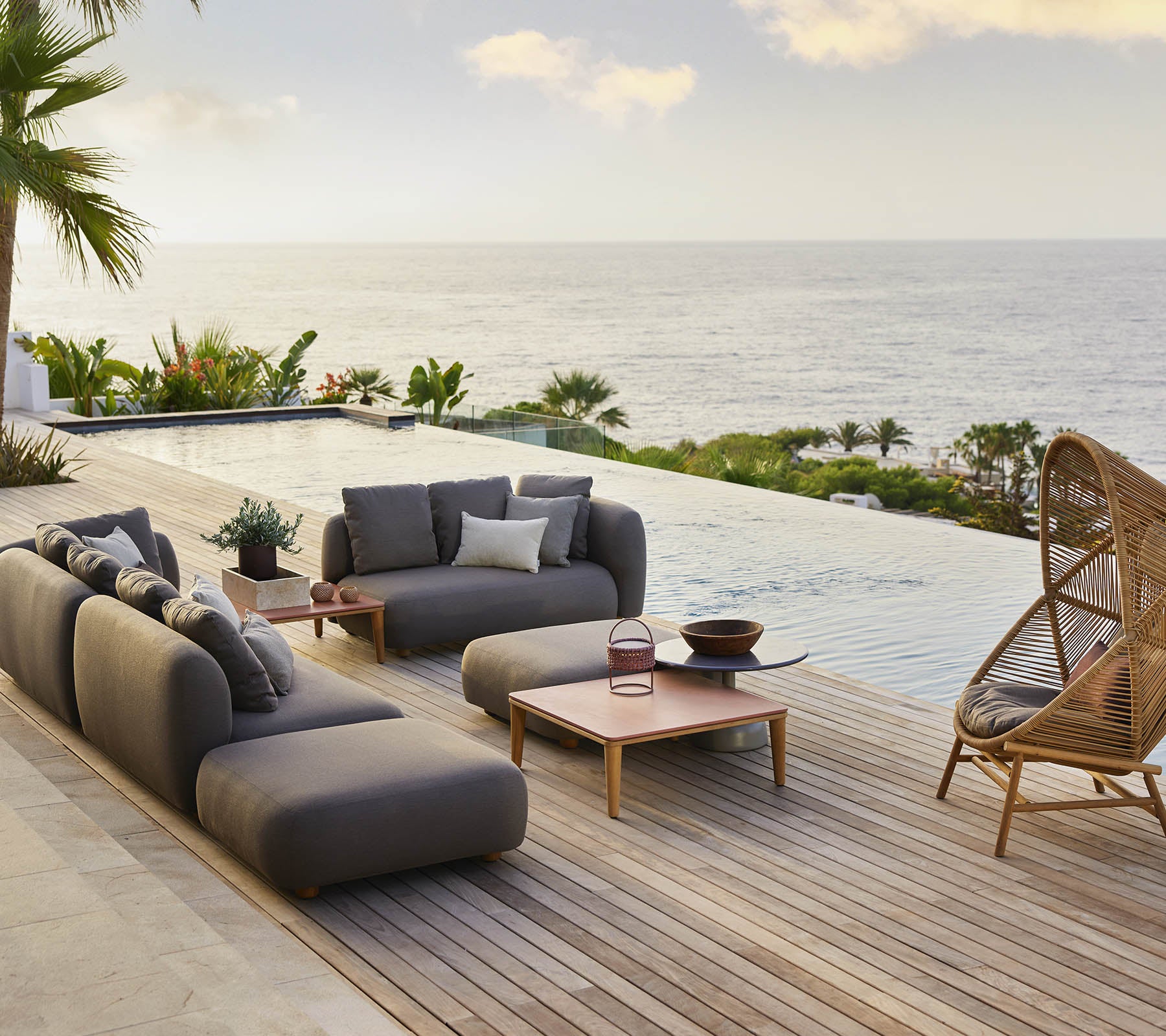 Stilrent loungeområde med en mysig hängstol i bikupform och moderna sittplatser, kompletterat med naturskön utsikt över havet och frodiga gröna omgivningar.