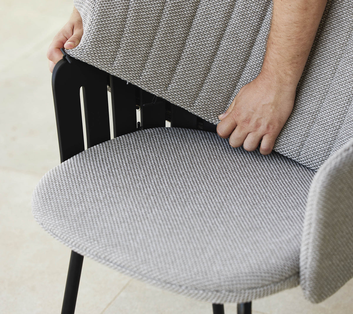 Person justerar ryggen på en modern stol med ett texturerat tygsäte, som visar en stilren design och ergonomiskt stöd.
