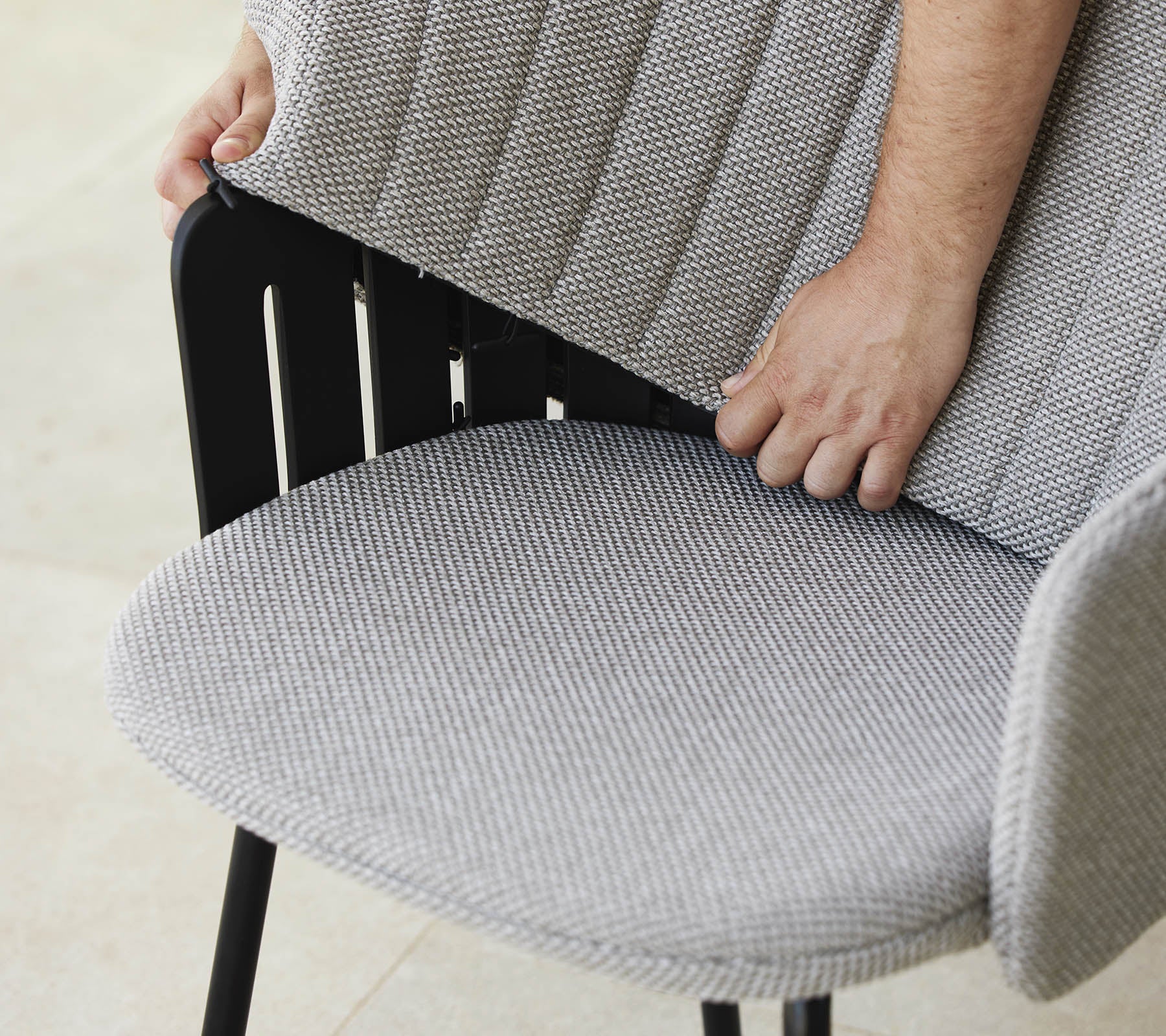 Person justerar ryggen på en modern stol med ett texturerat tygsäte, som visar en stilren design och ergonomiskt stöd.