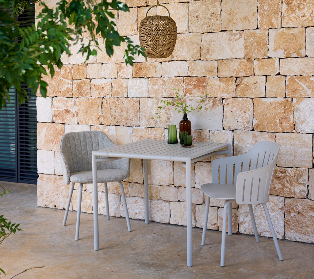 Modern grått bord och stolar med gröna och bruna flaskor i en utomhusmiljö.