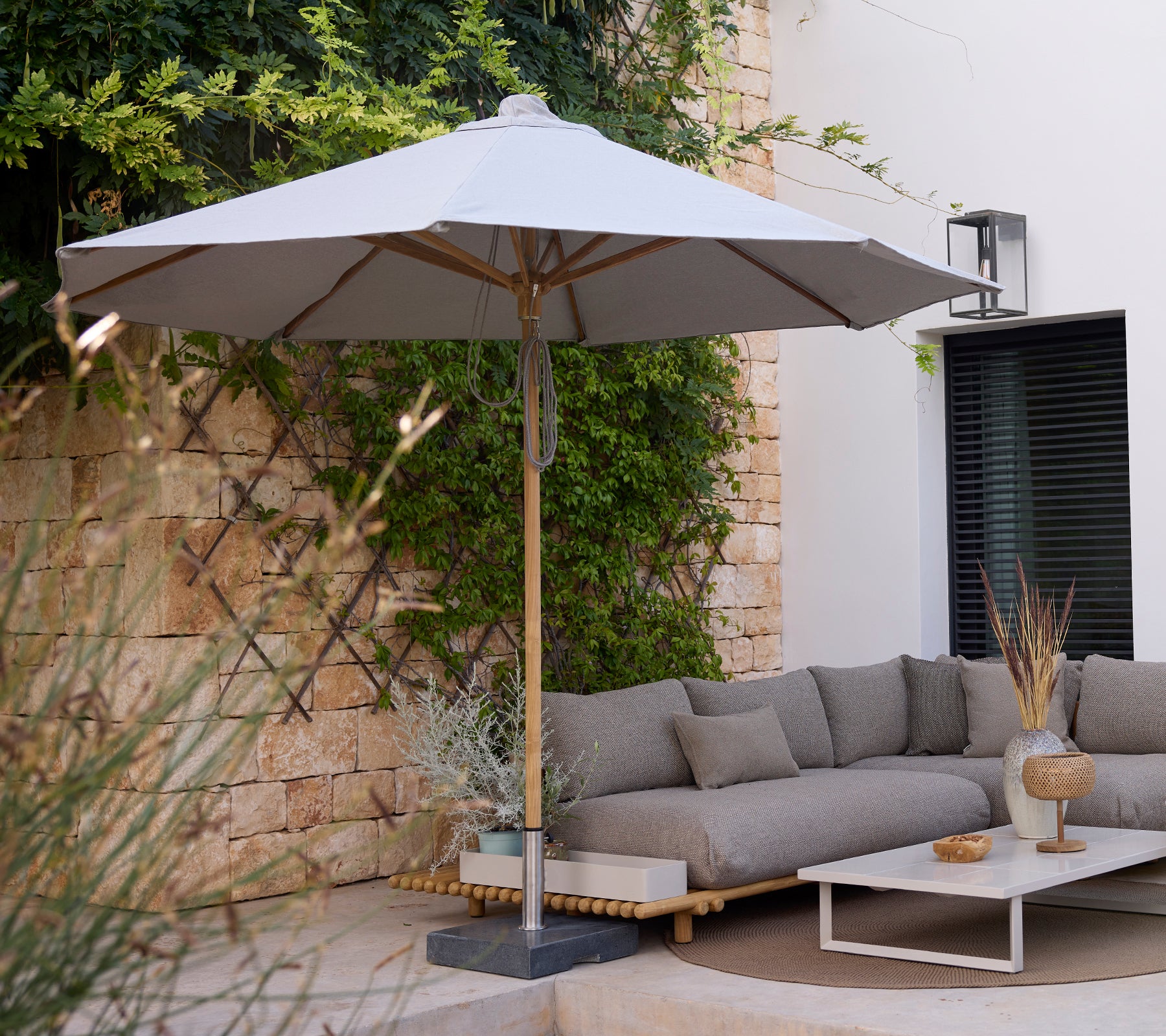 Modern loungeområde med en grå soffa, vitt bord och grå parasoll.