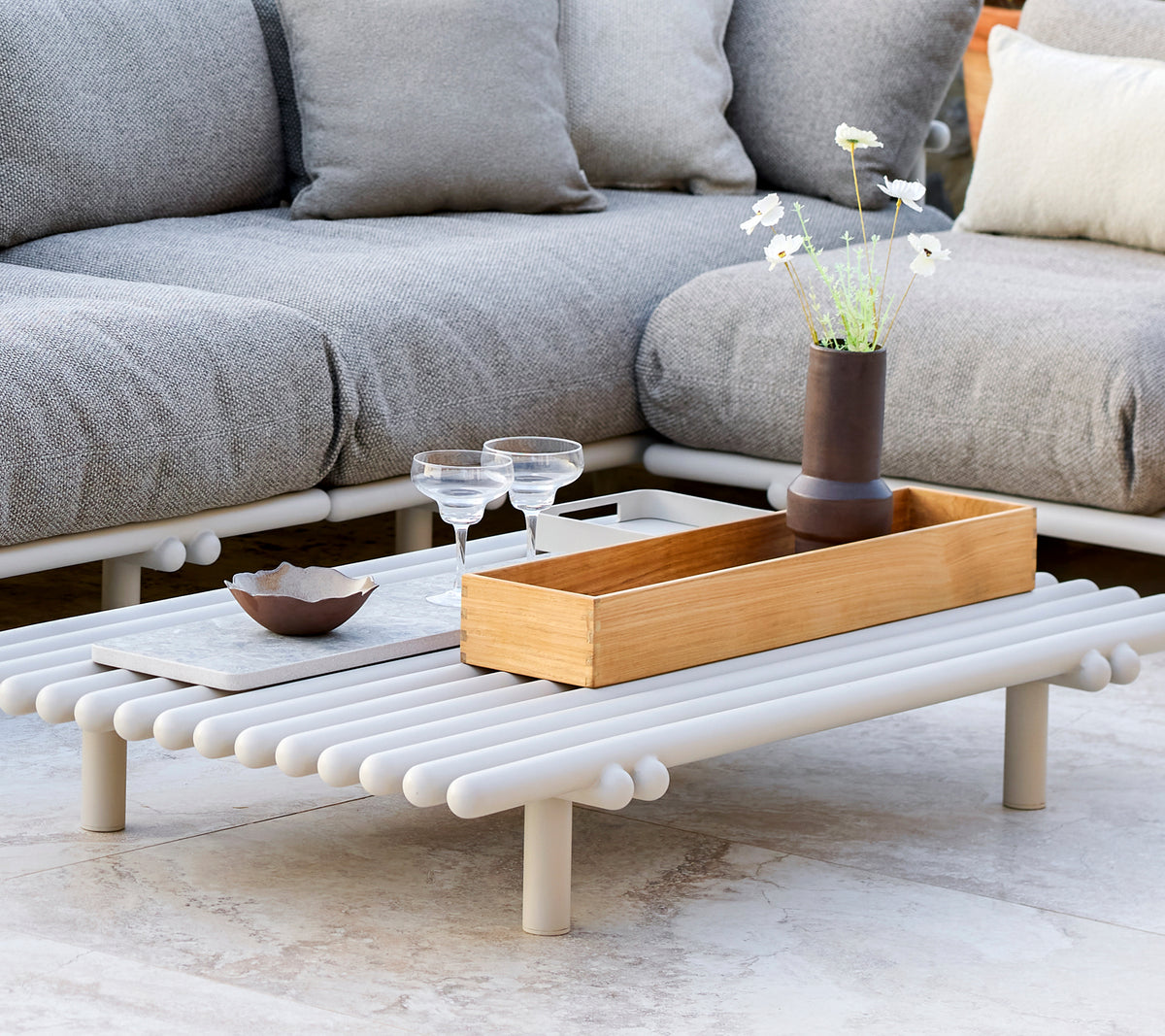 Ett stiligt soffbord med en teakförvaringslåda, med en minimalistisk design och dekorativa inslag som glas och en liten vas.