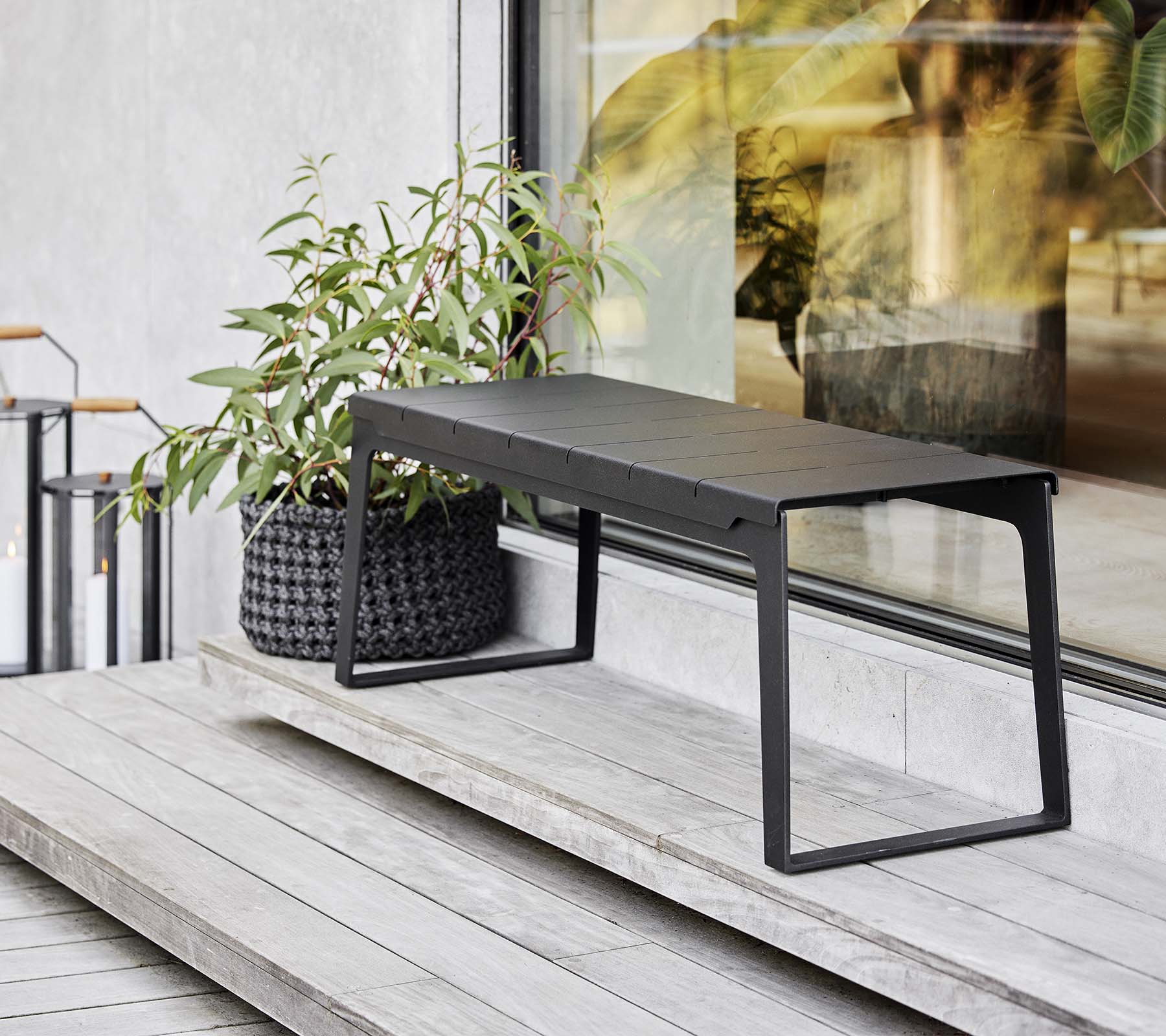 En sleek svart bänk placerad bredvid en planter med grönska, som visar moderna designelement och minimalistisk estetik.