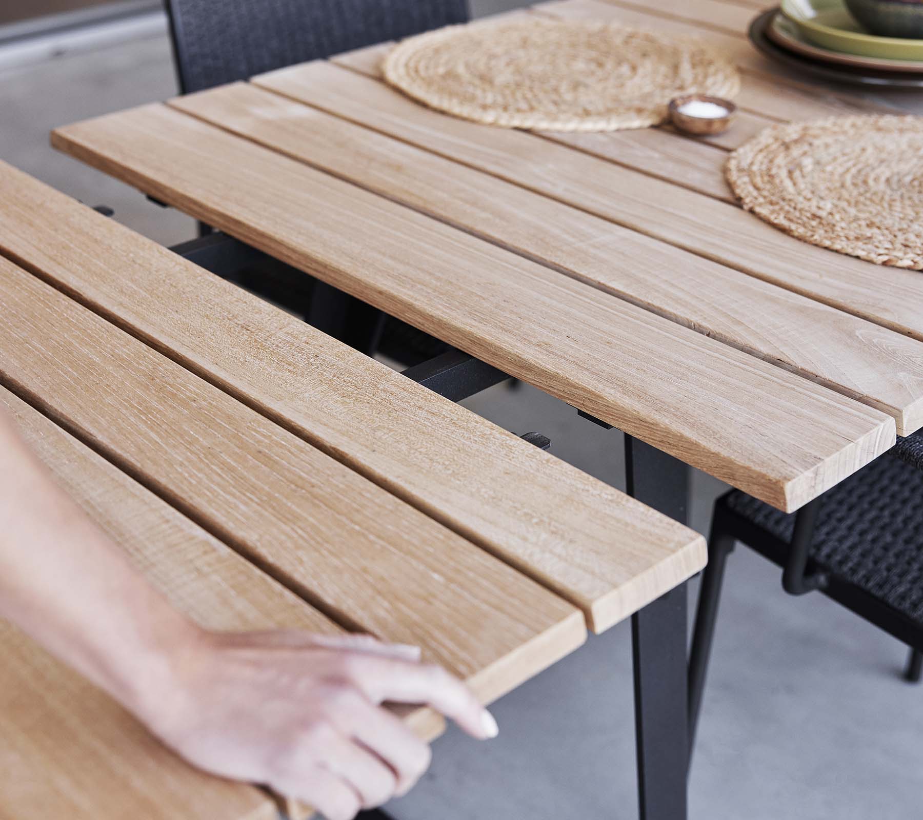 Detalj av ett träbord med lamelldesign, placemats och en minimalistisk estetik, perfekt för middagar eller sammankomster.